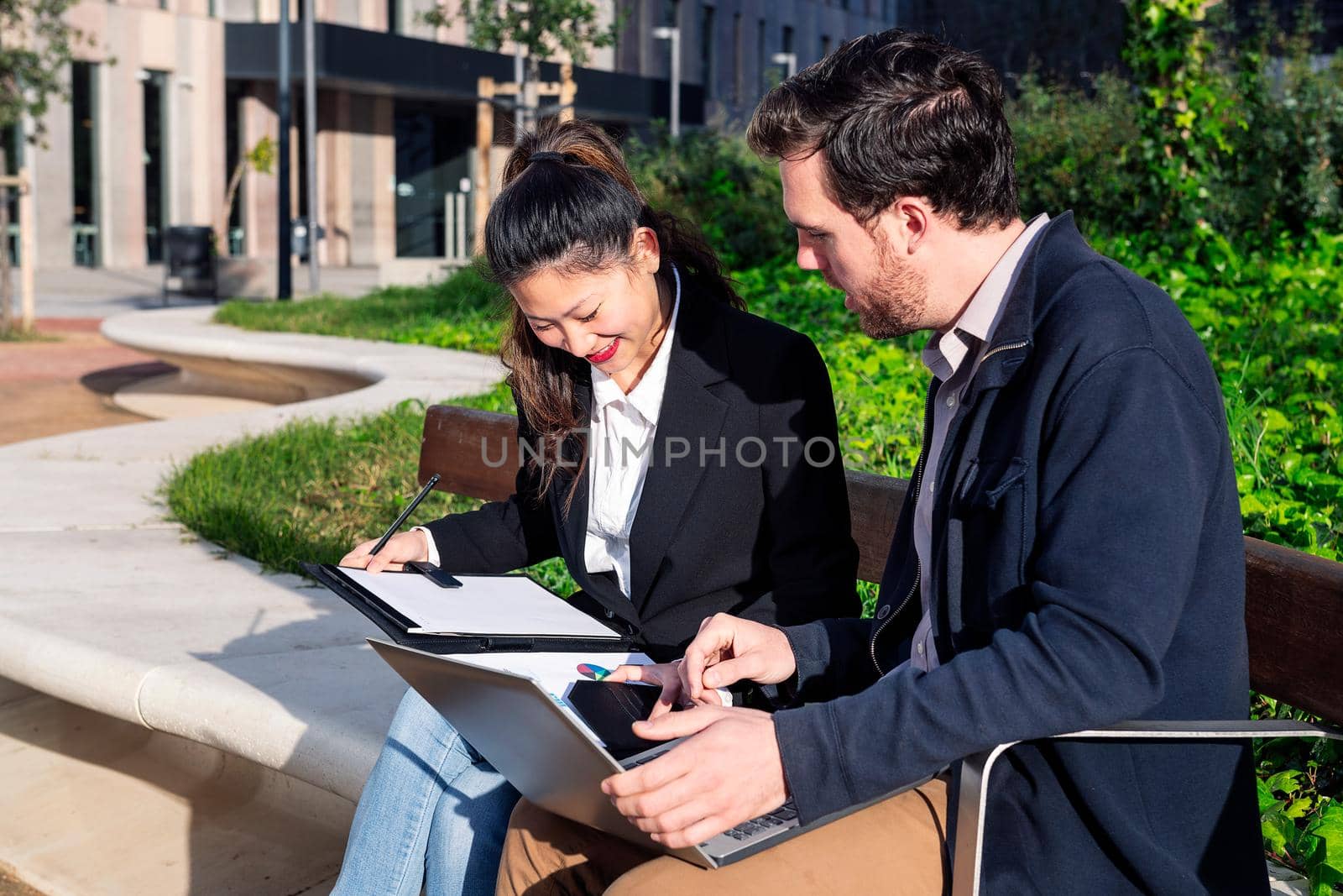 business partners working together with laptop in a park next to the office, concept of coworkers and diversity at work, copy space for text