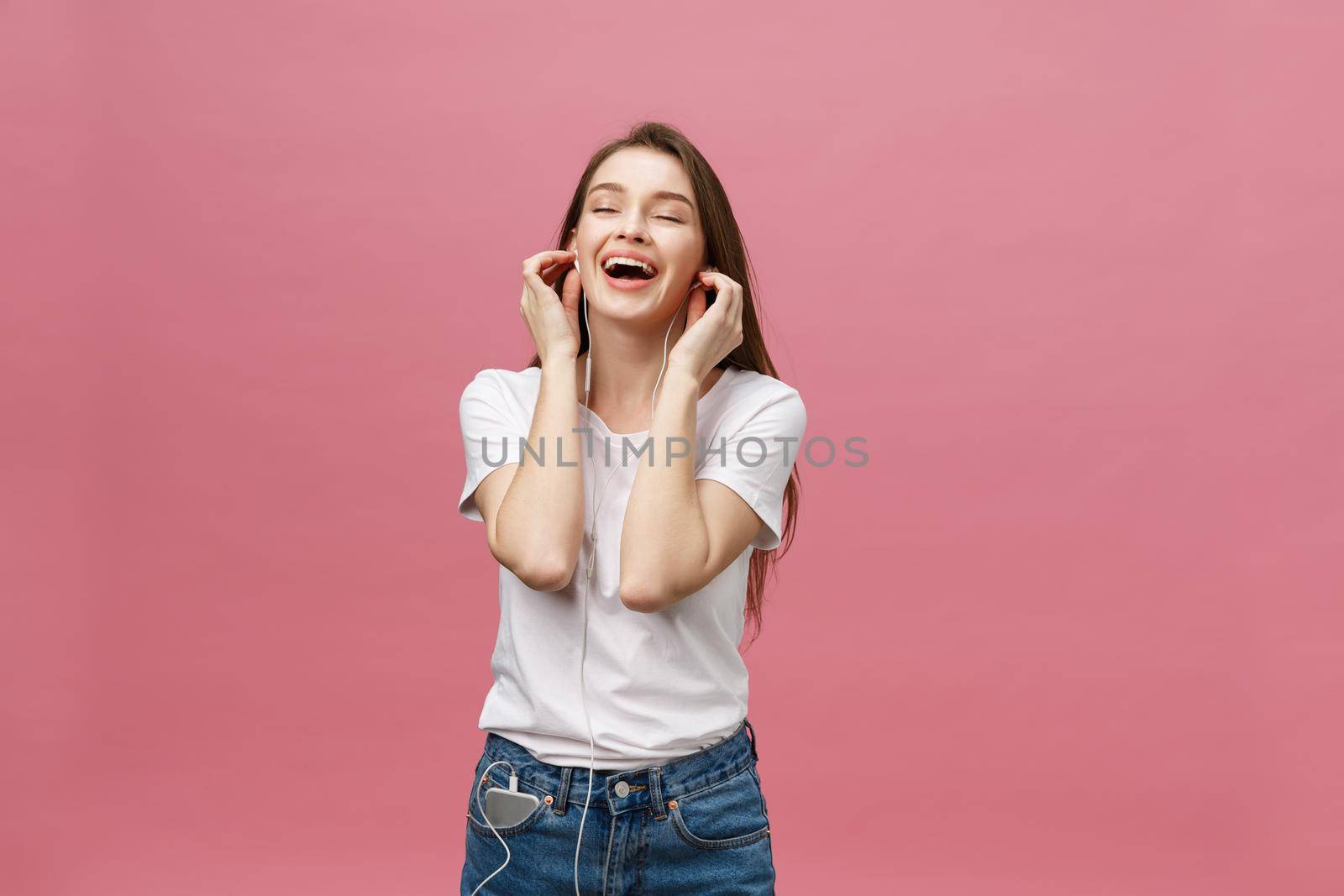 Lifestyle Concept. Young woman using phone for listening to music on pink background.