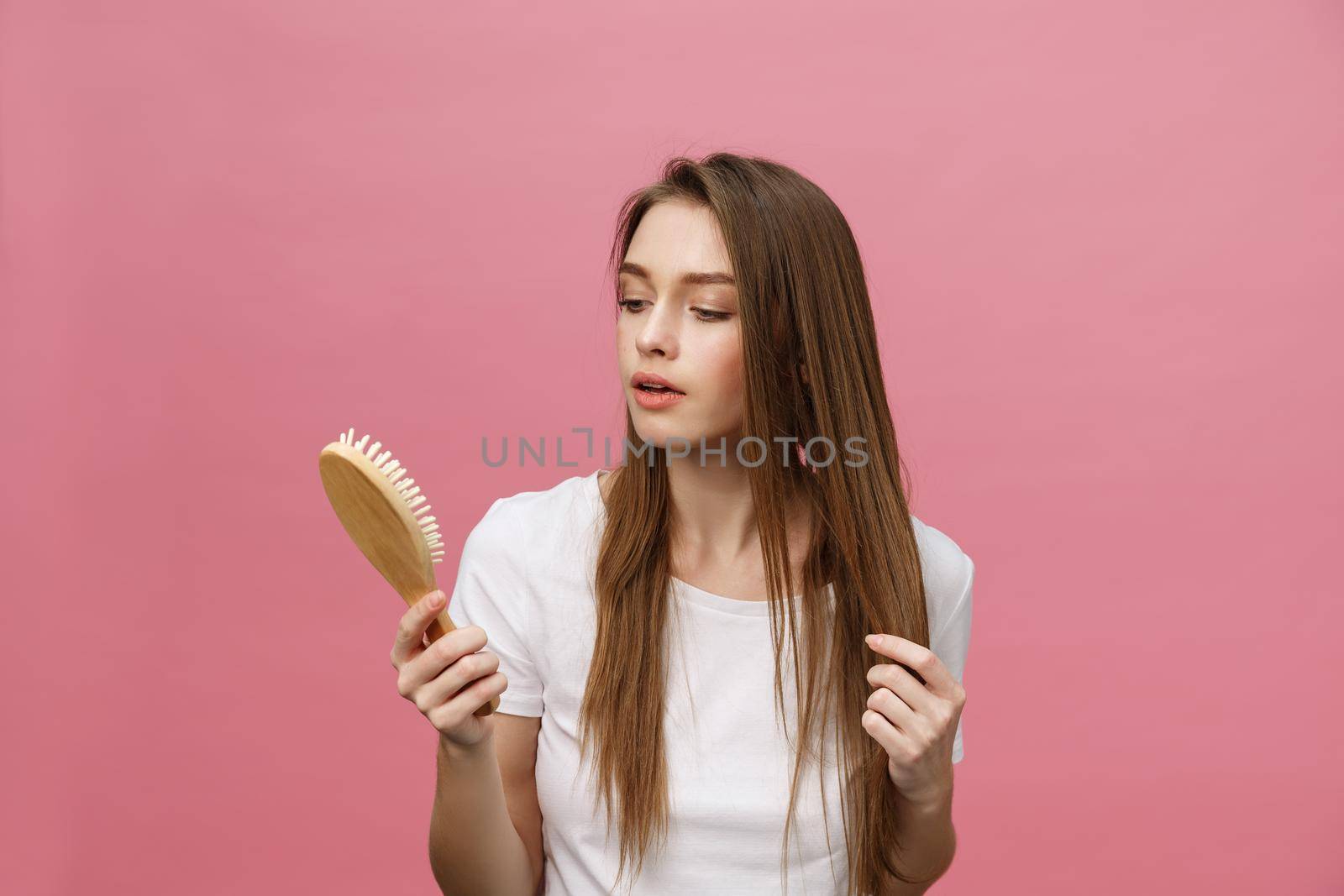 Smiling young woman combing hair and looking away isolated on pink by Benzoix