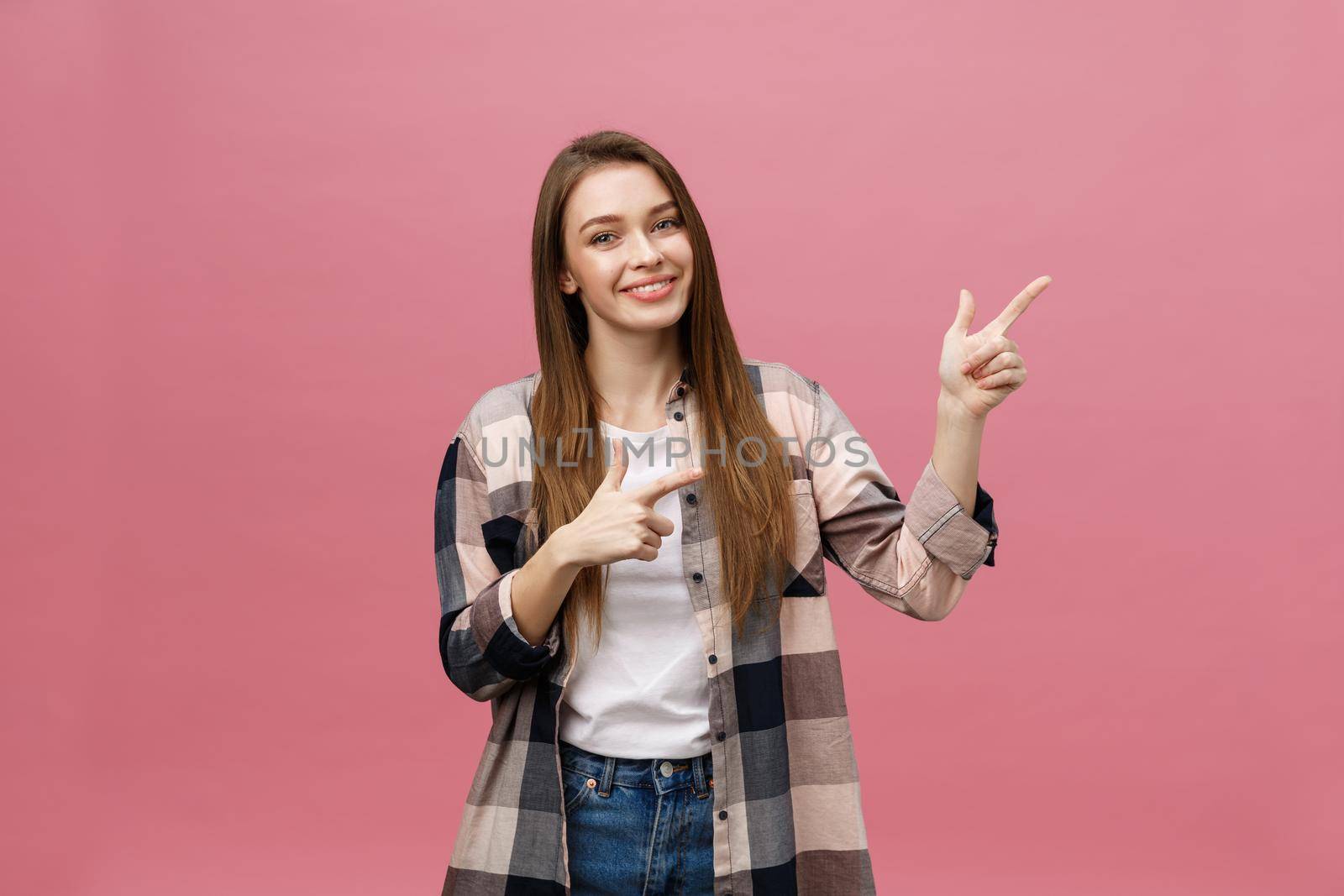 Cute young woman points a finger away isolate over pink background. Copy Space