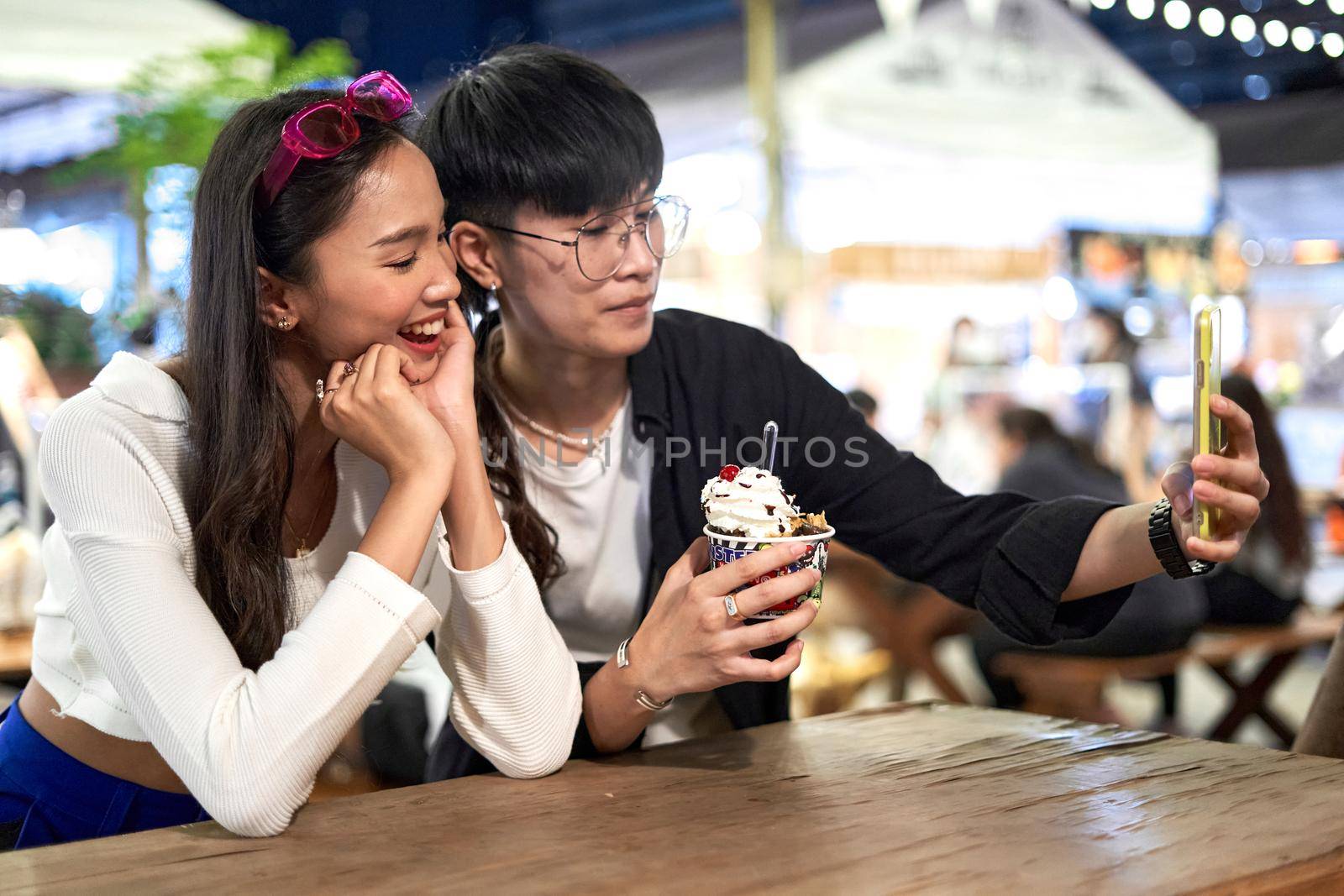 Lesbian couple eating an ice-cream while taking a selfie at a night fair by WesternExoticStockers