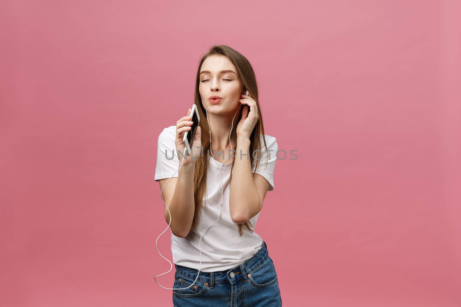 Lifestyle Concept. Young woman using phone for listening to music on pink background by Benzoix