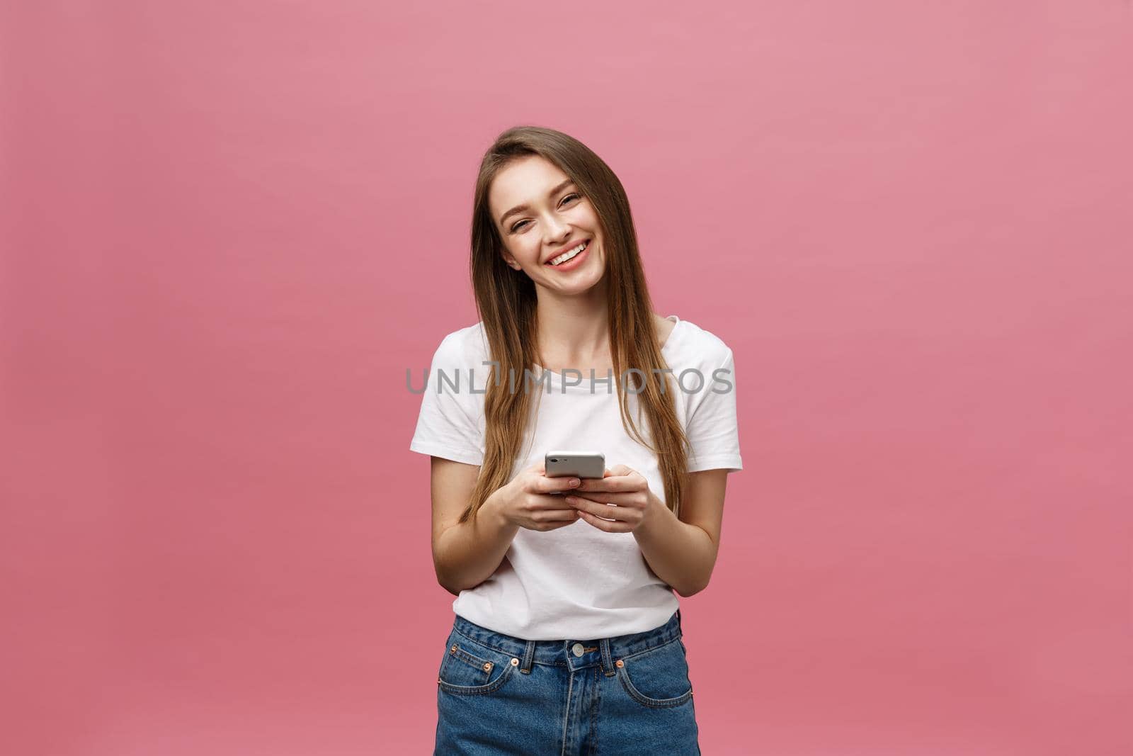 Photo of cheerful cute beautiful young woman chatting by mobile phone isolated over pink wall background. by Benzoix