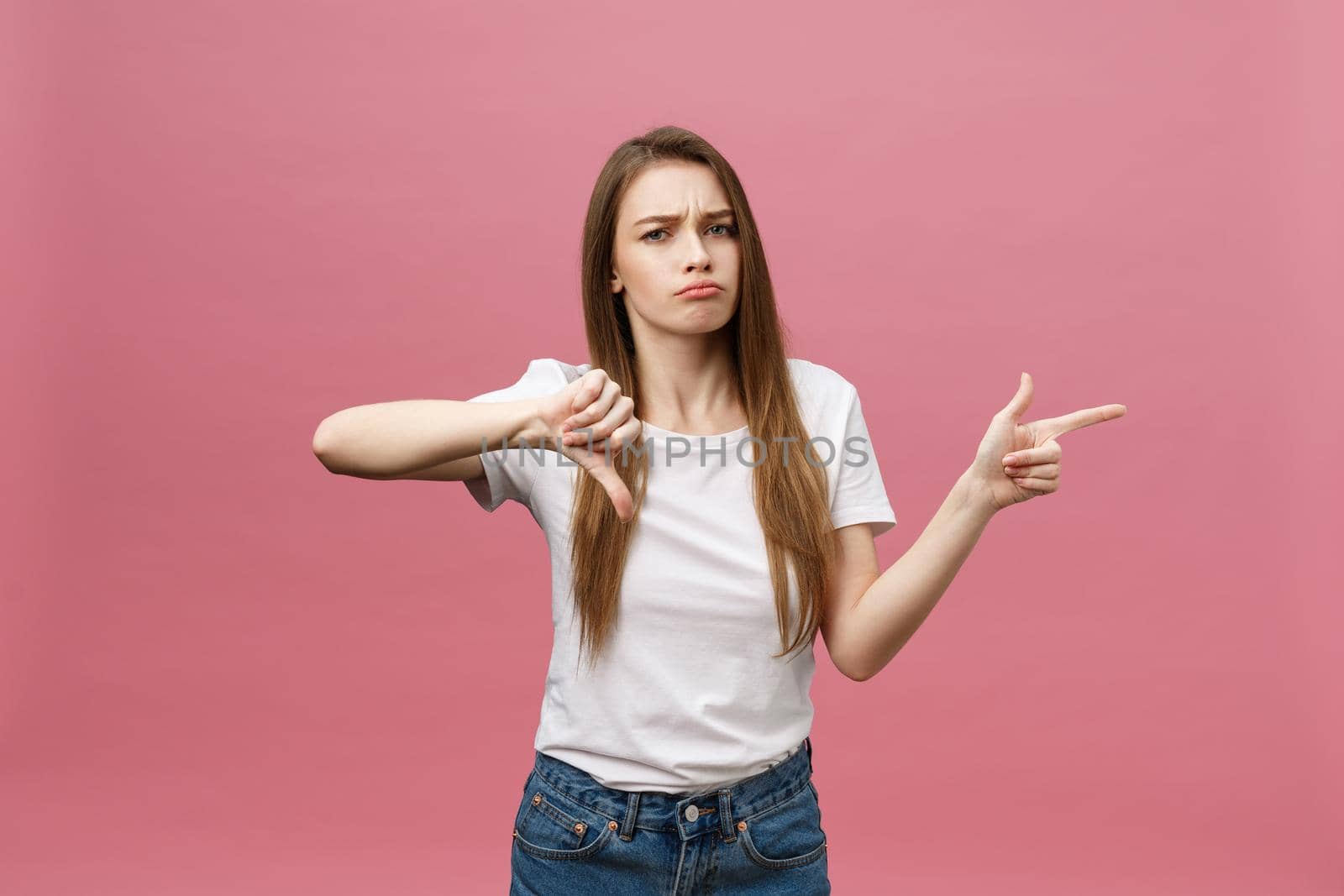 Closeup of serious strict young woman wears white shirt looks stressed and pointing up with finger isolated over pink background by Benzoix