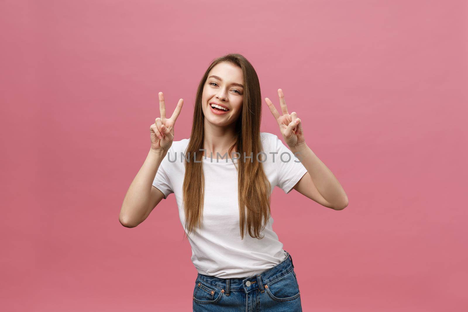 Portrait of a cheerful trendy woman showing two fingers sign over pink background.