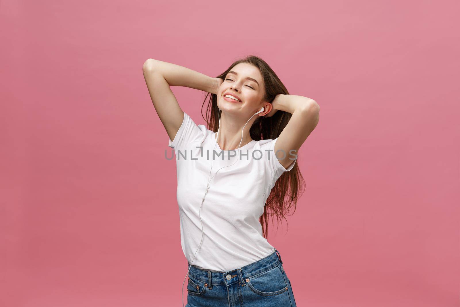 Lifestyle Concept. Young woman using phone for listening to music on pink background.