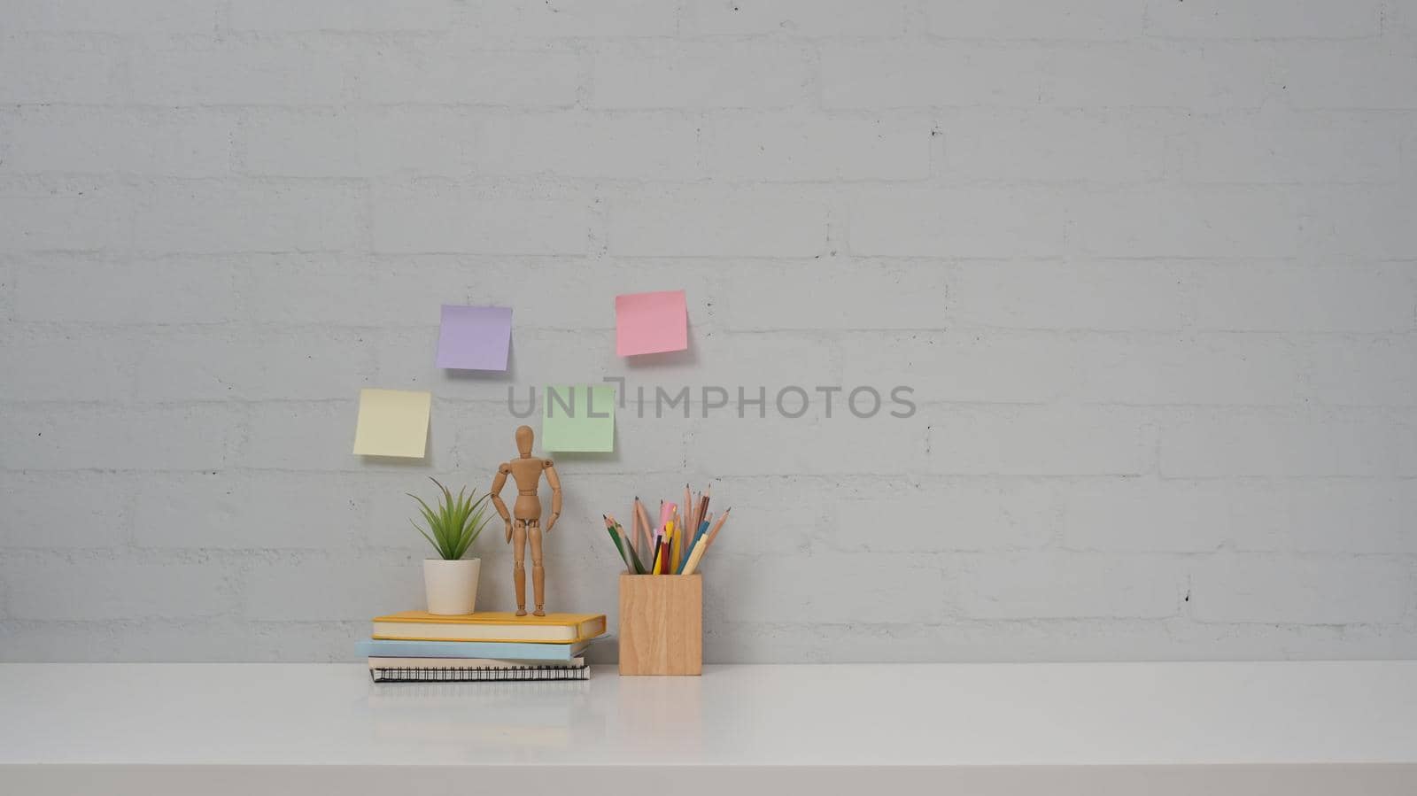 Personal accessories on white table and colorful sticky notes on brick wall background. Copy space for your advertise tex.