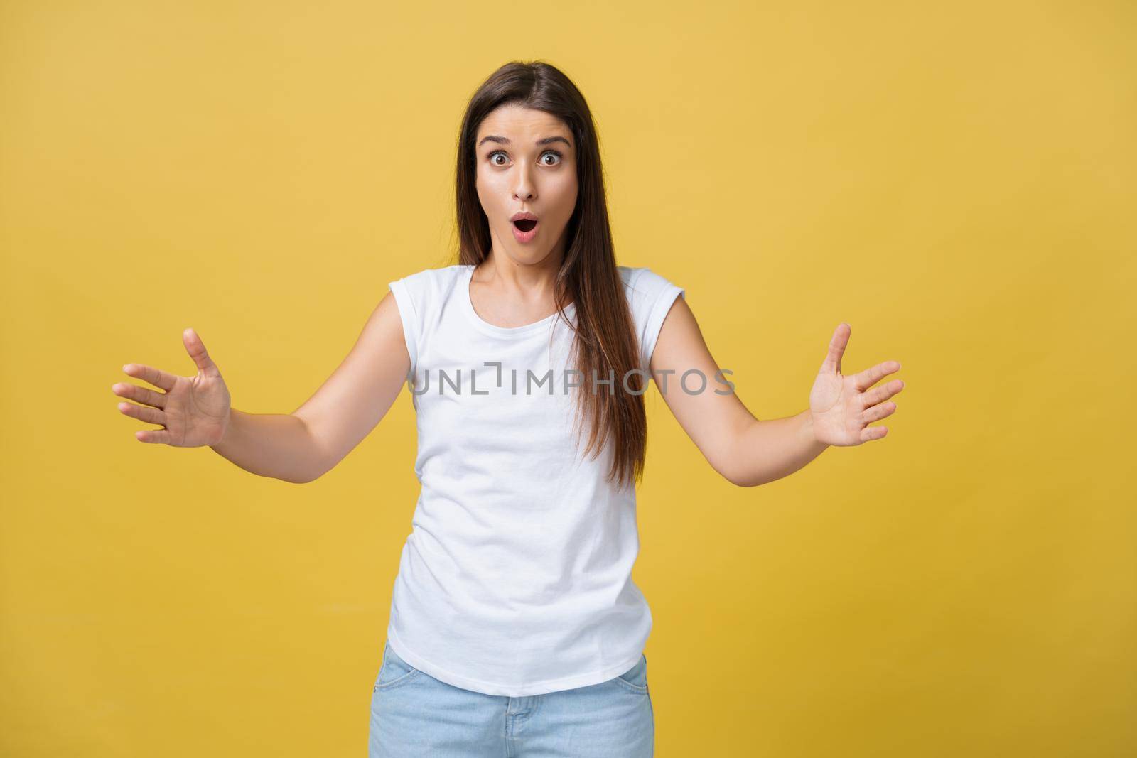 Beautiful female half-length portrait isolated on yellow studio backgroud. The young emotional smiling and surprised woman standing and looking at camera.The human emotions, facial expression concept.