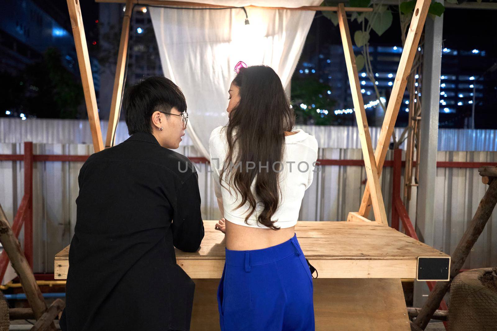 Two lesbian young women standing relaxed in a counter of a stall in a night fair by WesternExoticStockers