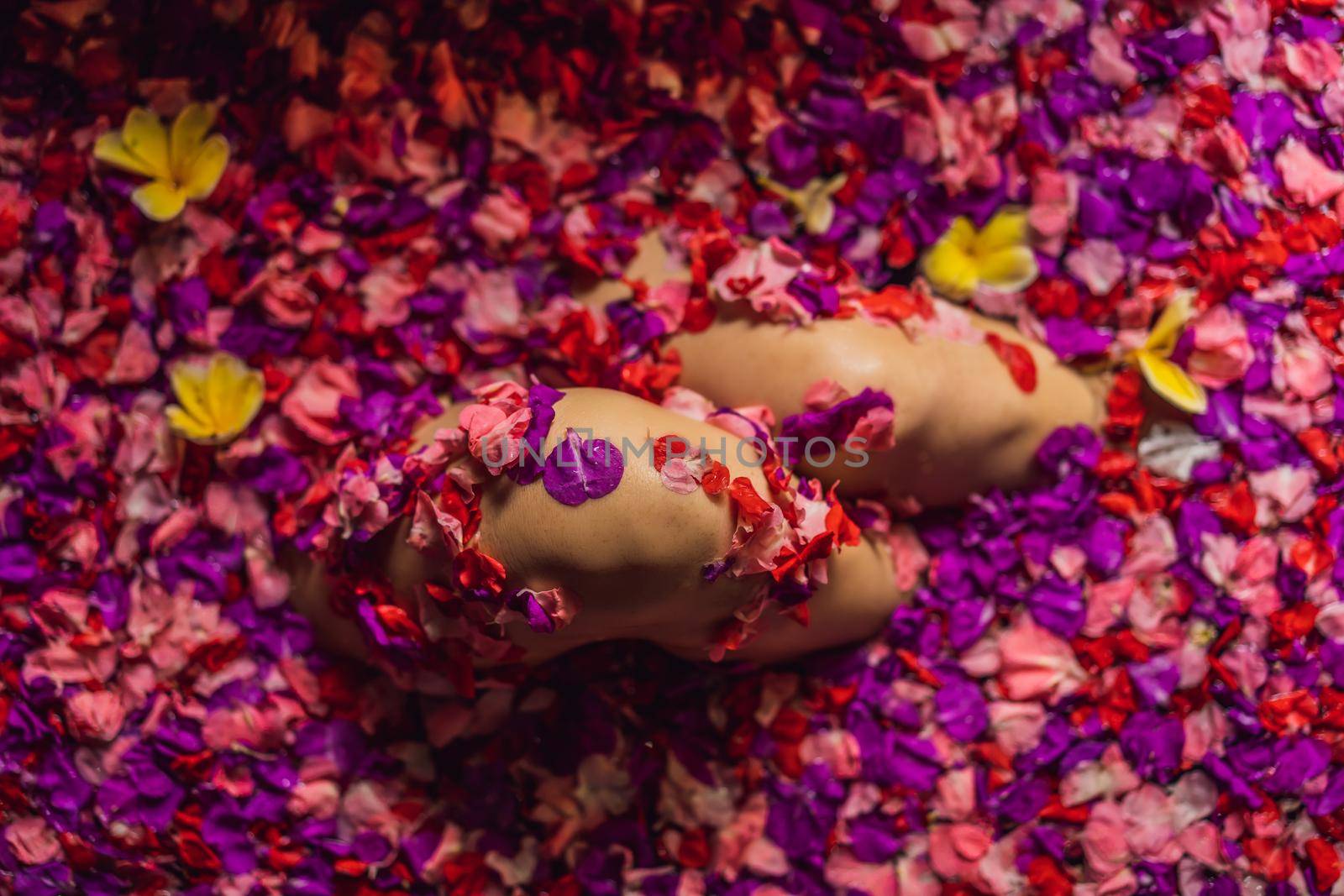 Attractive Young woman in bath with petals of tropical flowers and aroma oils. Spa treatments for skin rejuvenation. Alluring woman in Spa salon. Girl relaxing in bathtub with flower petals. Luxury.