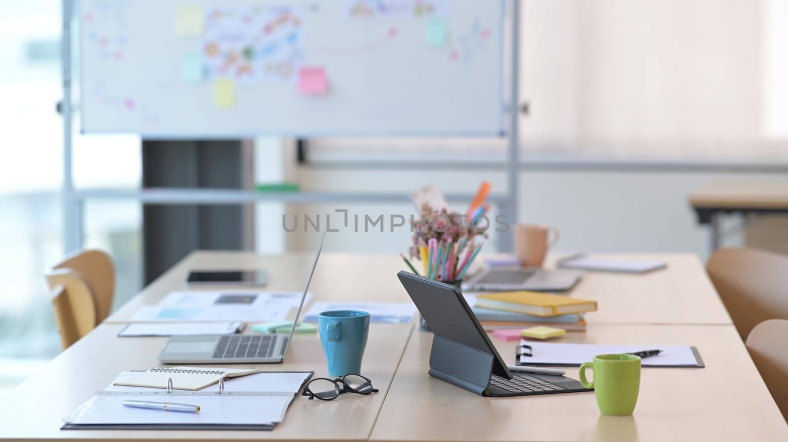 Computer laptop, documents and coffee cup on wooden table at bright modern conference room.