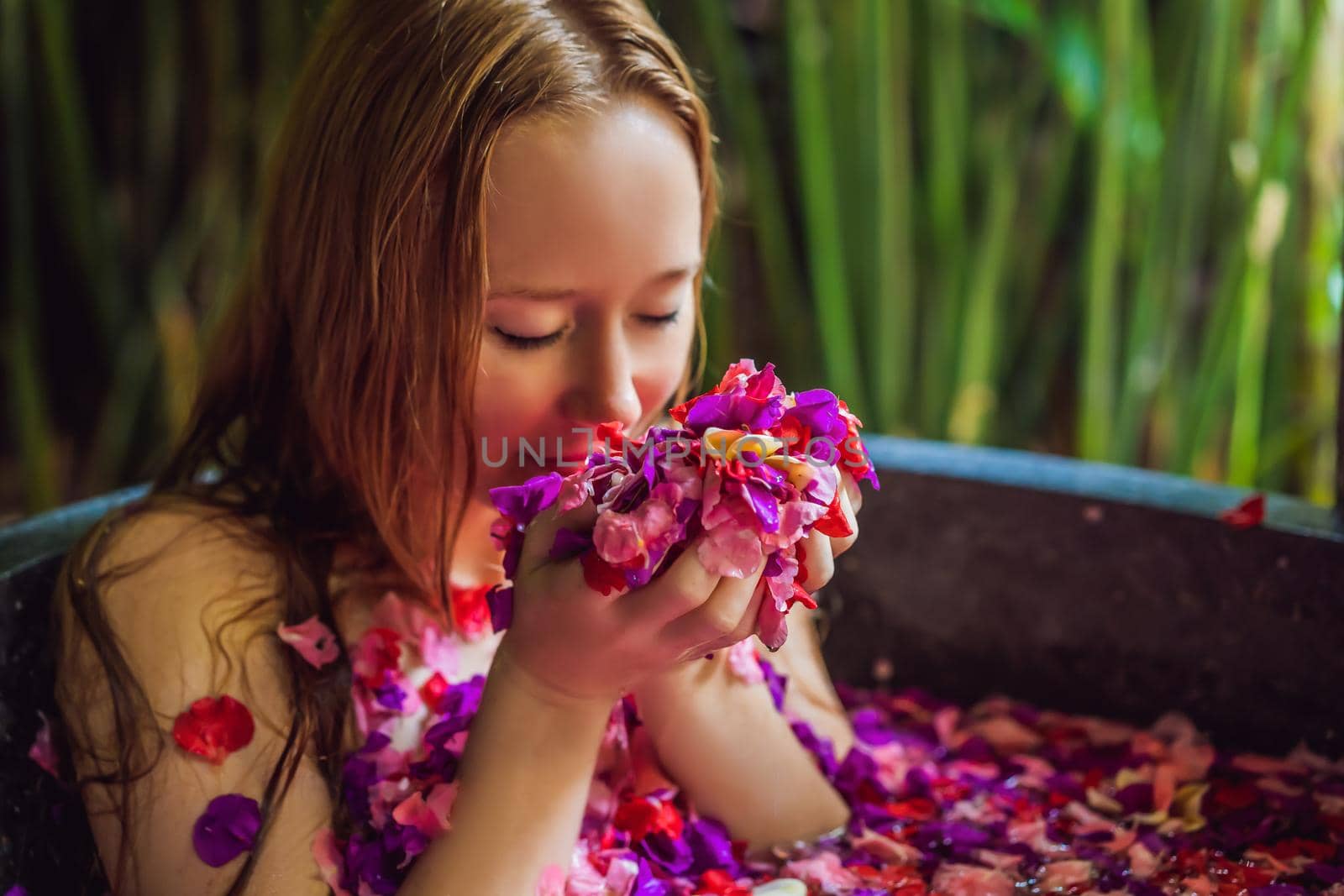 Attractive Young woman in bath with petals of tropical flowers and aroma oils. Spa treatments for skin rejuvenation. Alluring woman in Spa salon. Girl relaxing in bathtub with flower petals. Luxury.