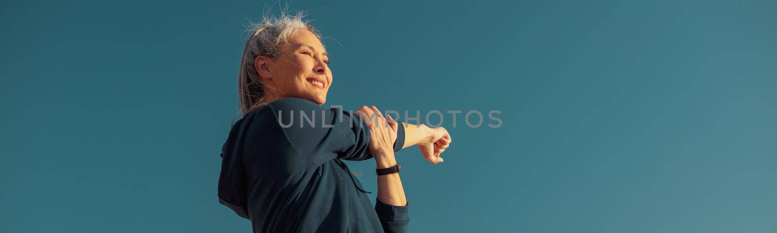 Strong female in sportswear doing arm workout on the sports ground on a sunny day by the waterfront