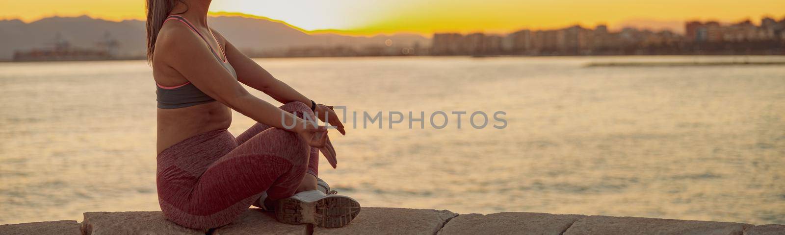 Asian sportswoman practicing yoga, sitting on edge at seashore by Yaroslav_astakhov