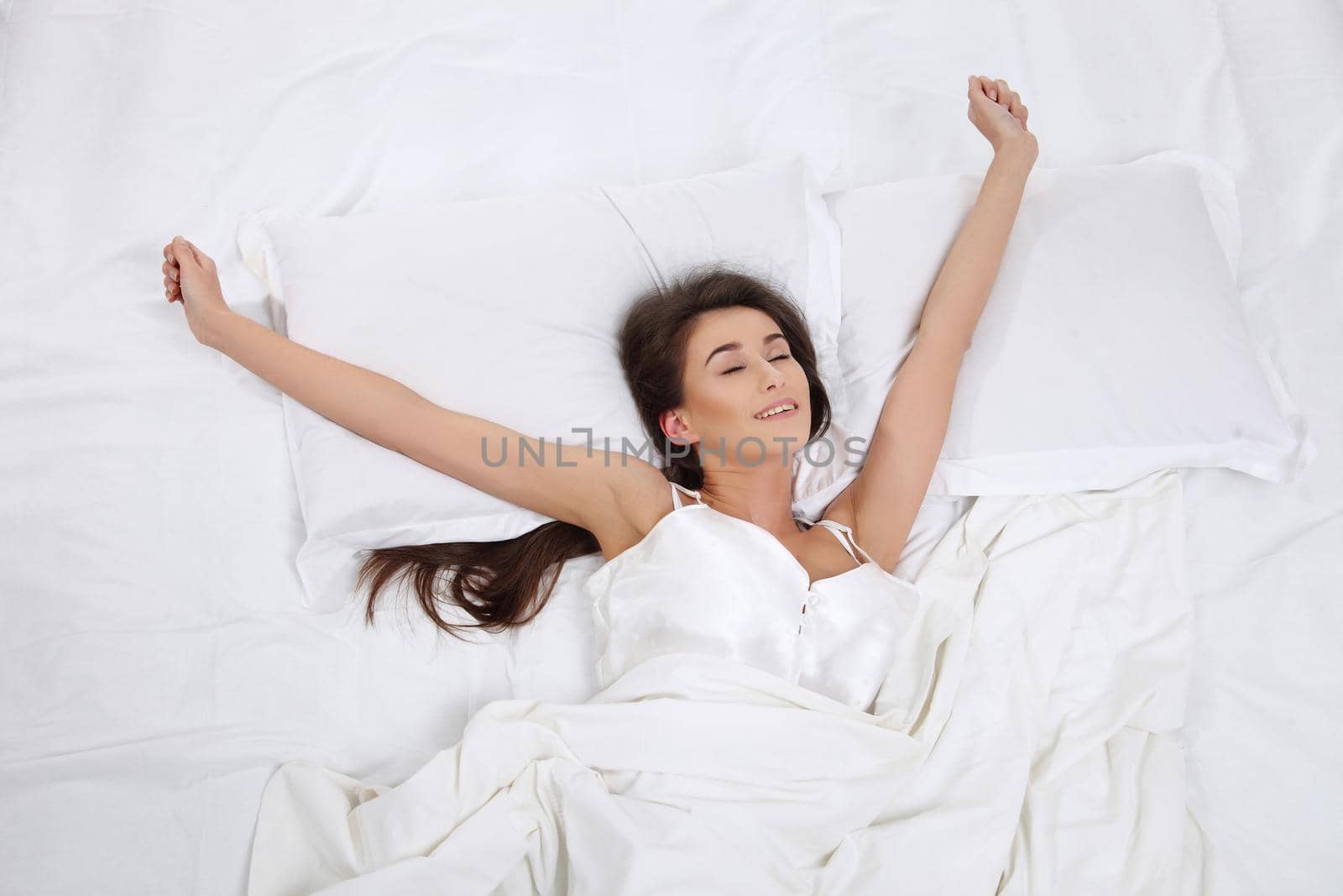 Young beautiful woman waking up in her bed fully rested. Woman stretching in bed after wake up. Healthy lifestyle. Wellness concept