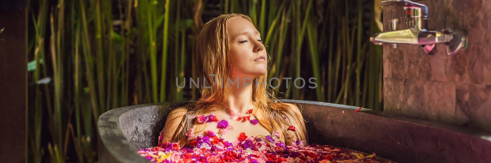 Attractive Young woman in bath with petals of tropical flowers and aroma oils. Spa treatments for skin rejuvenation. Alluring woman in Spa salon. Girl relaxing in bathtub with flower petals. Luxury. BANNER, LONG FORMAT