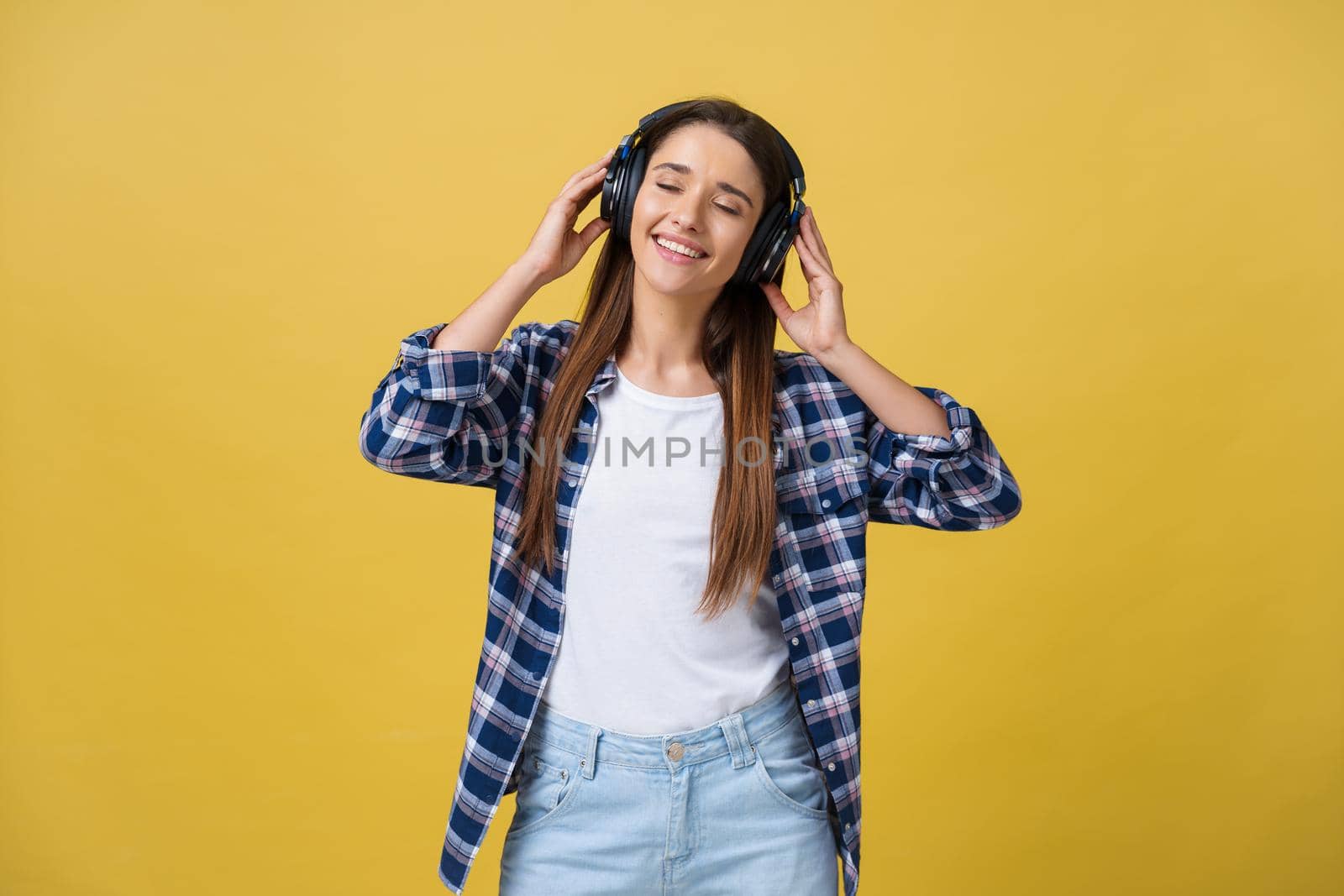 Beautiful calm young woman listening the music in headphone with closed eyes on yellow background. Closeup.