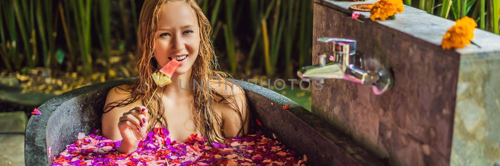 Attractive Young woman in bath with petals of tropical flowers and aroma oils. Spa treatments for skin rejuvenation. Alluring woman in Spa salon. Girl relaxing in bathtub with flower petals. Luxury. BANNER, LONG FORMAT