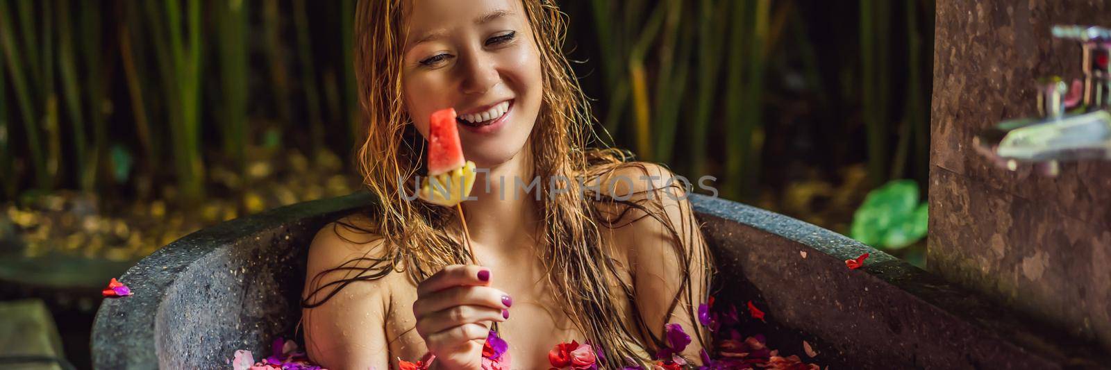 Attractive Young woman in bath with petals of tropical flowers and aroma oils. Spa treatments for skin rejuvenation. Alluring woman in Spa salon. Girl relaxing in bathtub with flower petals. Luxury. BANNER, LONG FORMAT