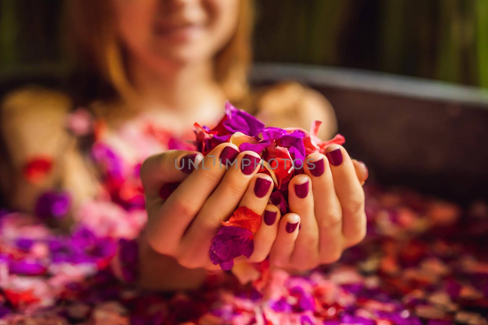 Attractive Young woman in bath with petals of tropical flowers and aroma oils. Spa treatments for skin rejuvenation. Alluring woman in Spa salon. Girl relaxing in bathtub with flower petals. Luxury.