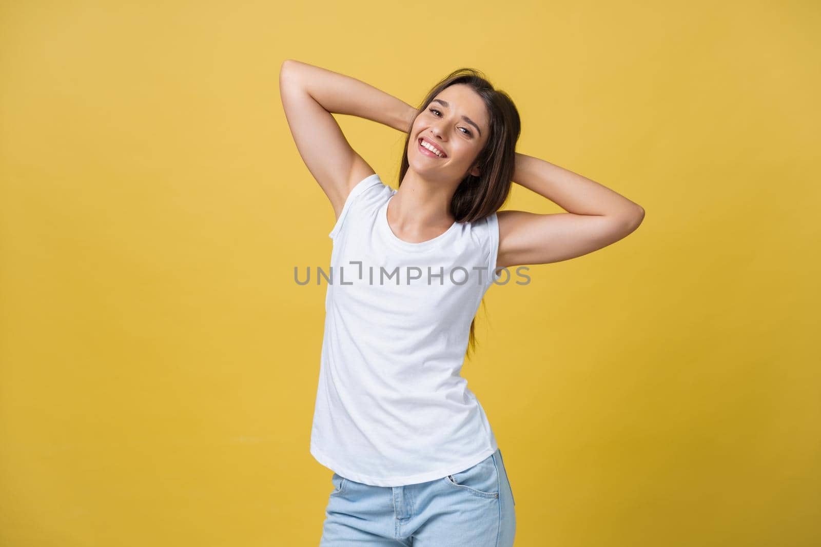 Close-up portrait of cute young woman relaxing with hand behind head. Isolated over yellow background