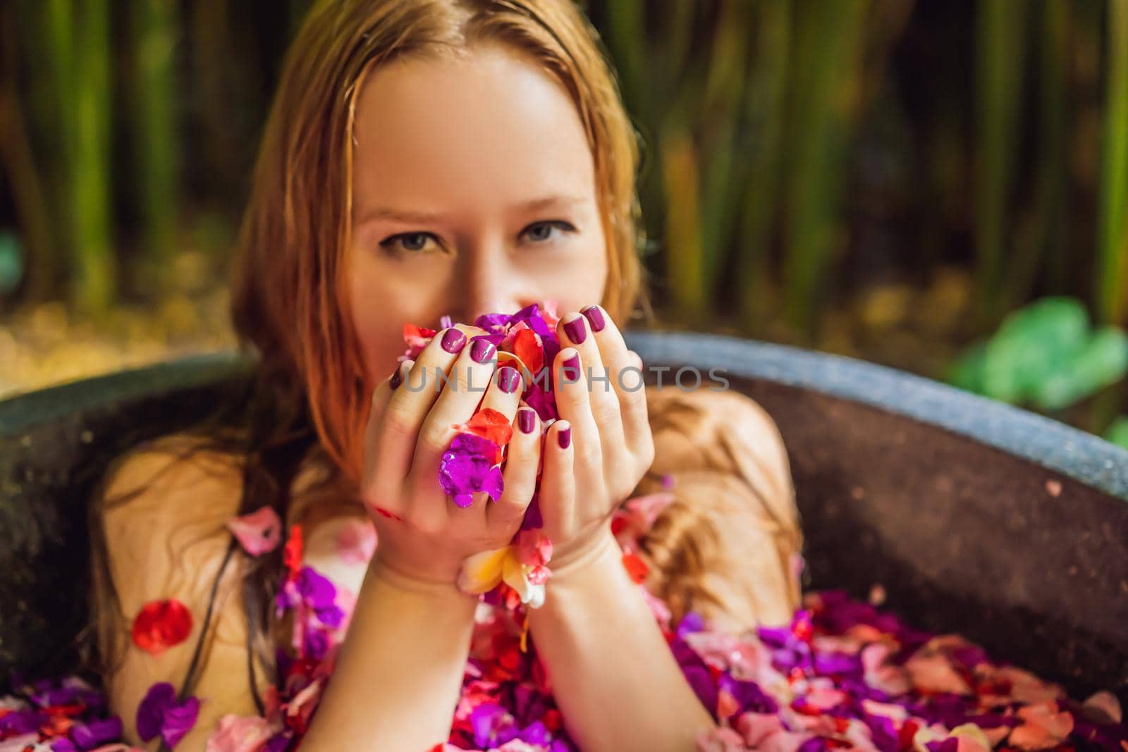 Attractive Young woman in bath with petals of tropical flowers and aroma oils. Spa treatments for skin rejuvenation. Alluring woman in Spa salon. Girl relaxing in bathtub with flower petals. Luxury.