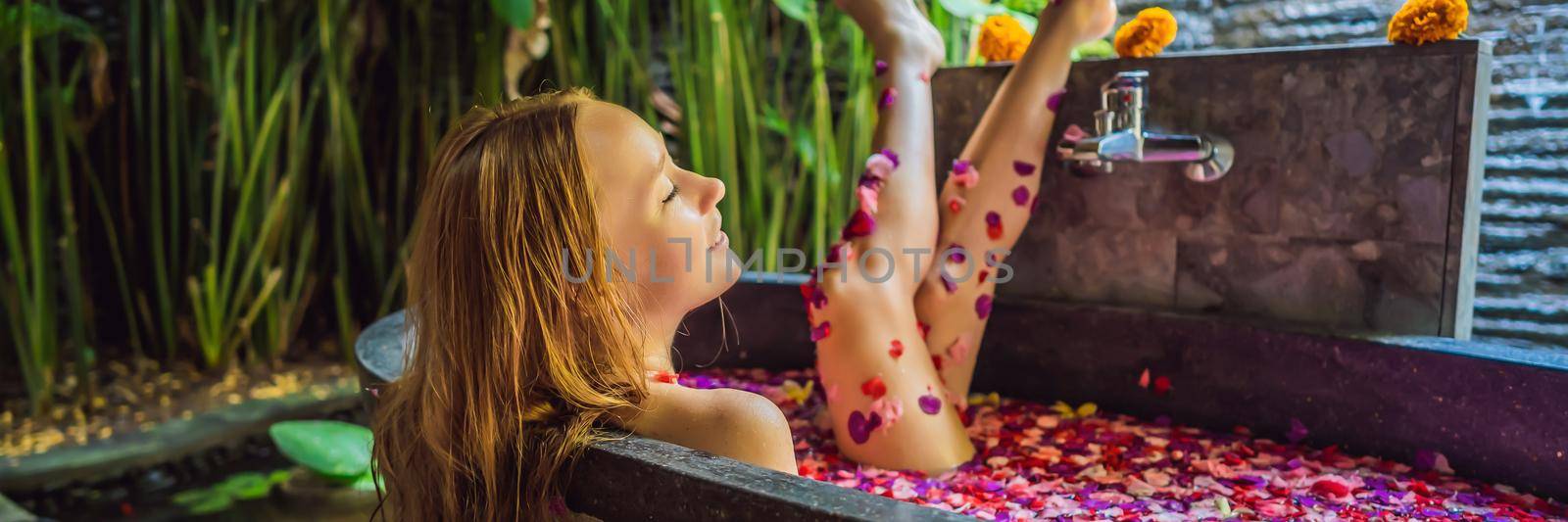 Attractive Young woman in bath with petals of tropical flowers and aroma oils. Spa treatments for skin rejuvenation. Alluring woman in Spa salon. Girl relaxing in bathtub with flower petals. Luxury. BANNER, LONG FORMAT