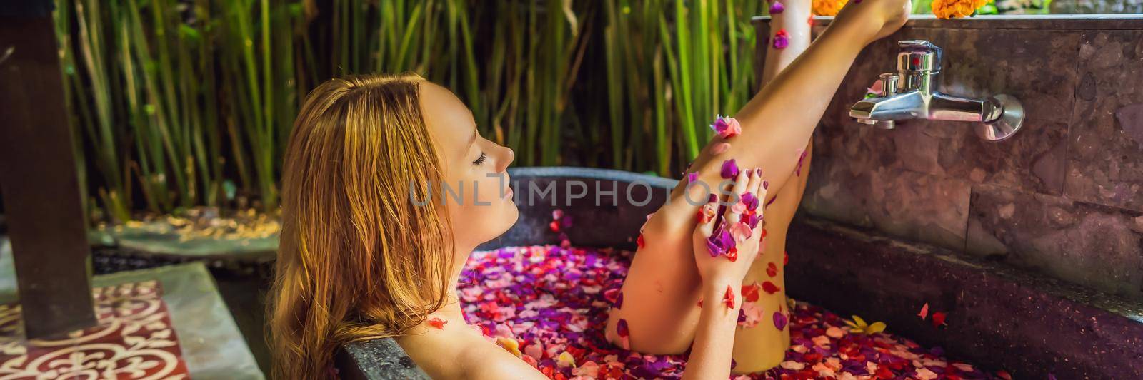 Attractive Young woman in bath with petals of tropical flowers and aroma oils. Spa treatments for skin rejuvenation. Alluring woman in Spa salon. Girl relaxing in bathtub with flower petals. Luxury. BANNER, LONG FORMAT