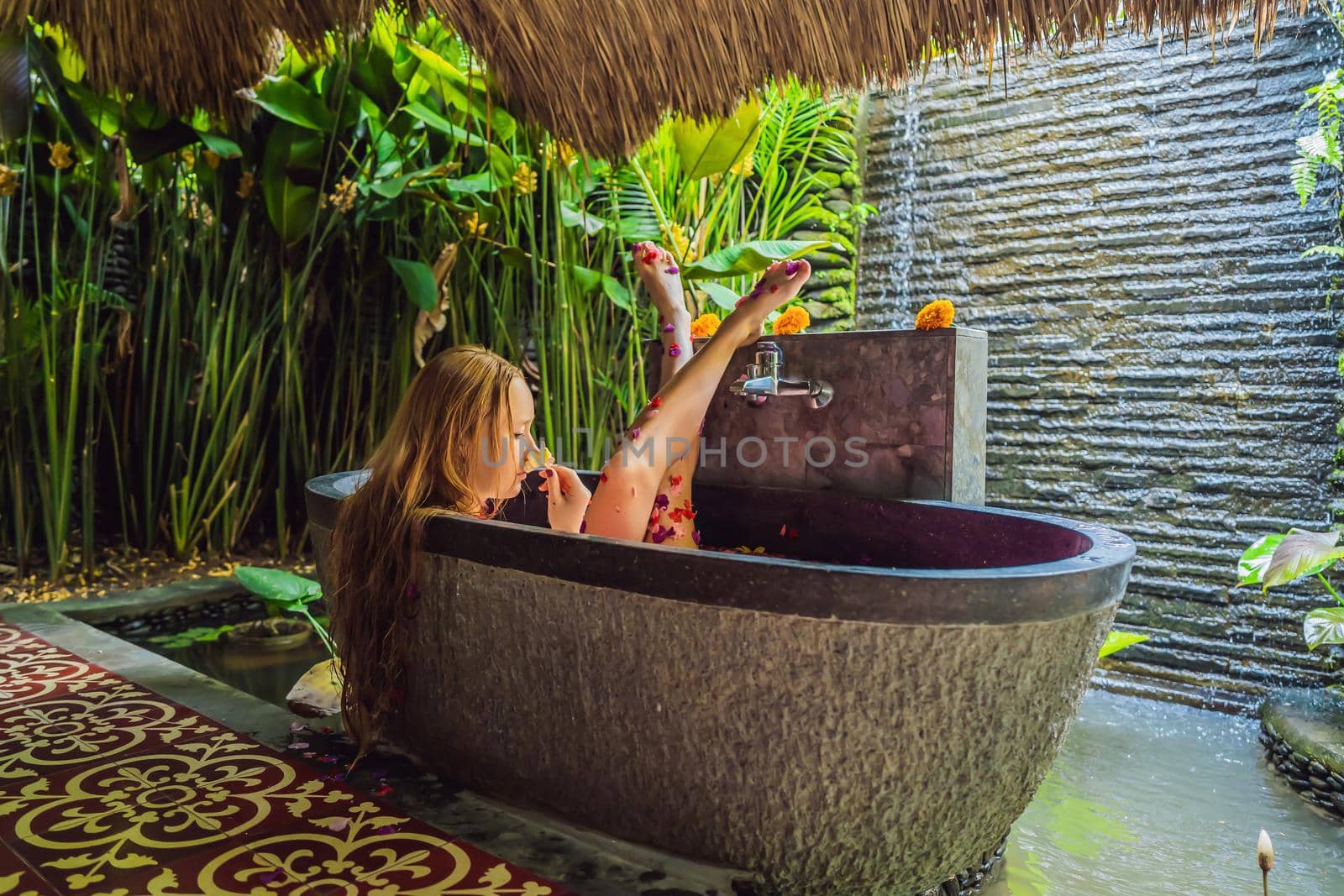 Attractive Young woman in bath with petals of tropical flowers and aroma oils. Spa treatments for skin rejuvenation. Alluring woman in Spa salon. Girl relaxing in bathtub with flower petals. Luxury.