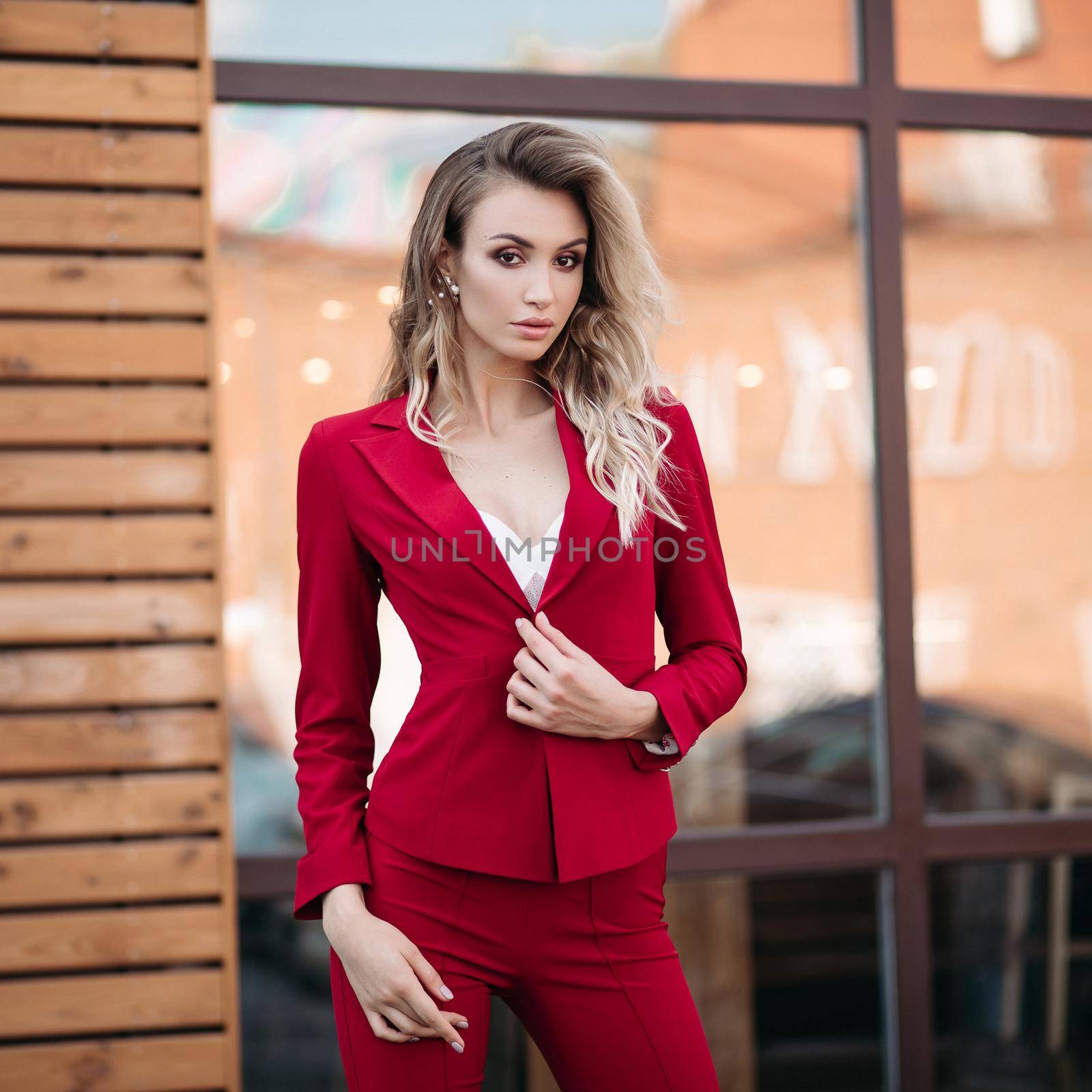elegant gorgeous blonde businesswoman in expensive dark red jacket and trousers with golden buttons on sleeves. She is standing with arms crossed.