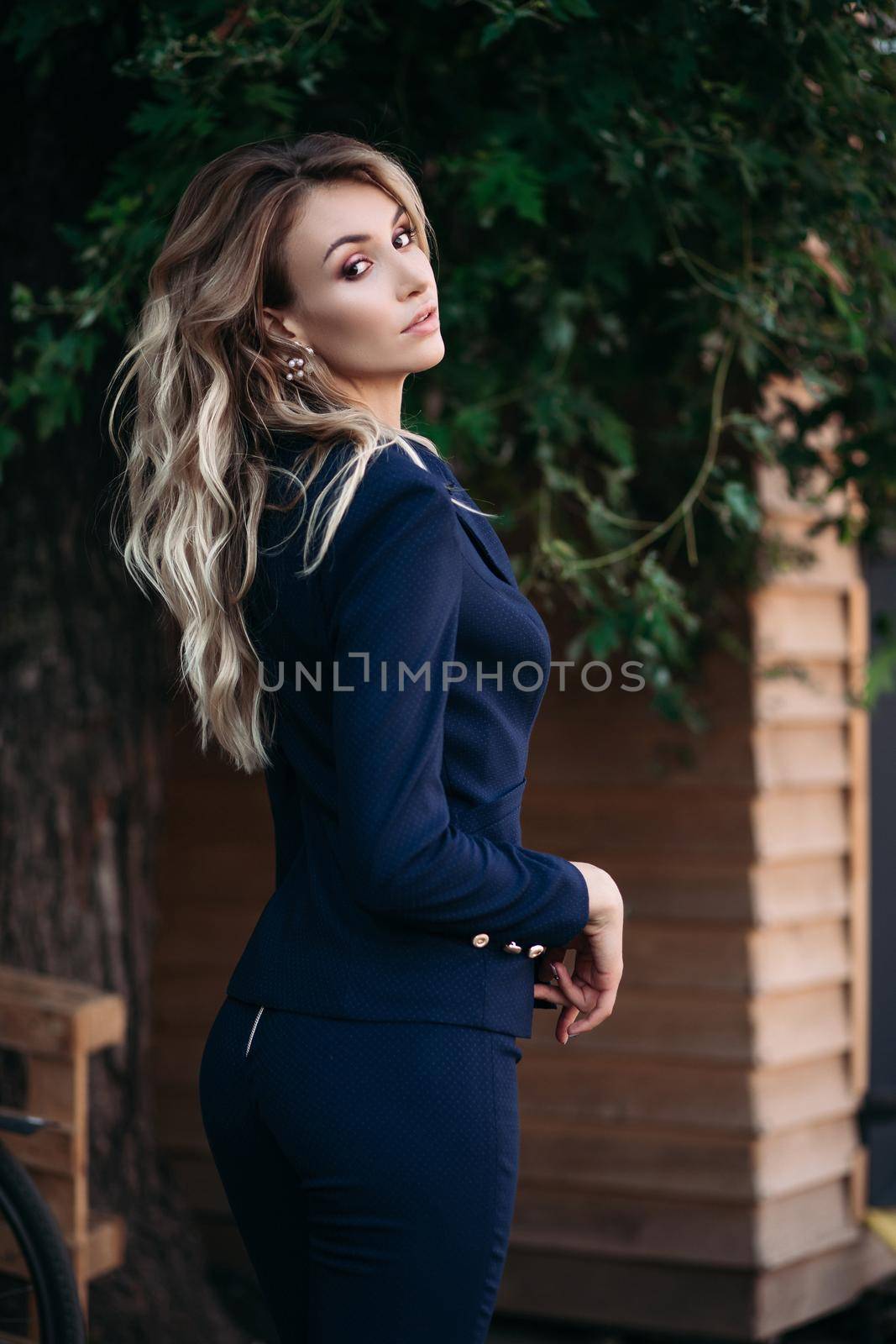 elegant gorgeous blonde businesswoman in expensive dark black jacket and trousers with golden buttons on sleeves. She is standing with arms crossed.