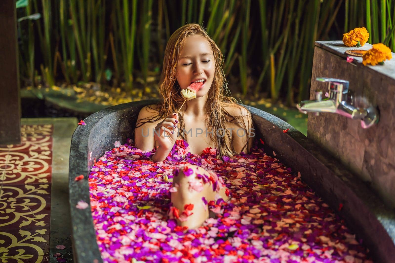 Attractive Young woman in bath with petals of tropical flowers and aroma oils. Spa treatments for skin rejuvenation. Alluring woman in Spa salon. Girl relaxing in bathtub with flower petals. Luxury.
