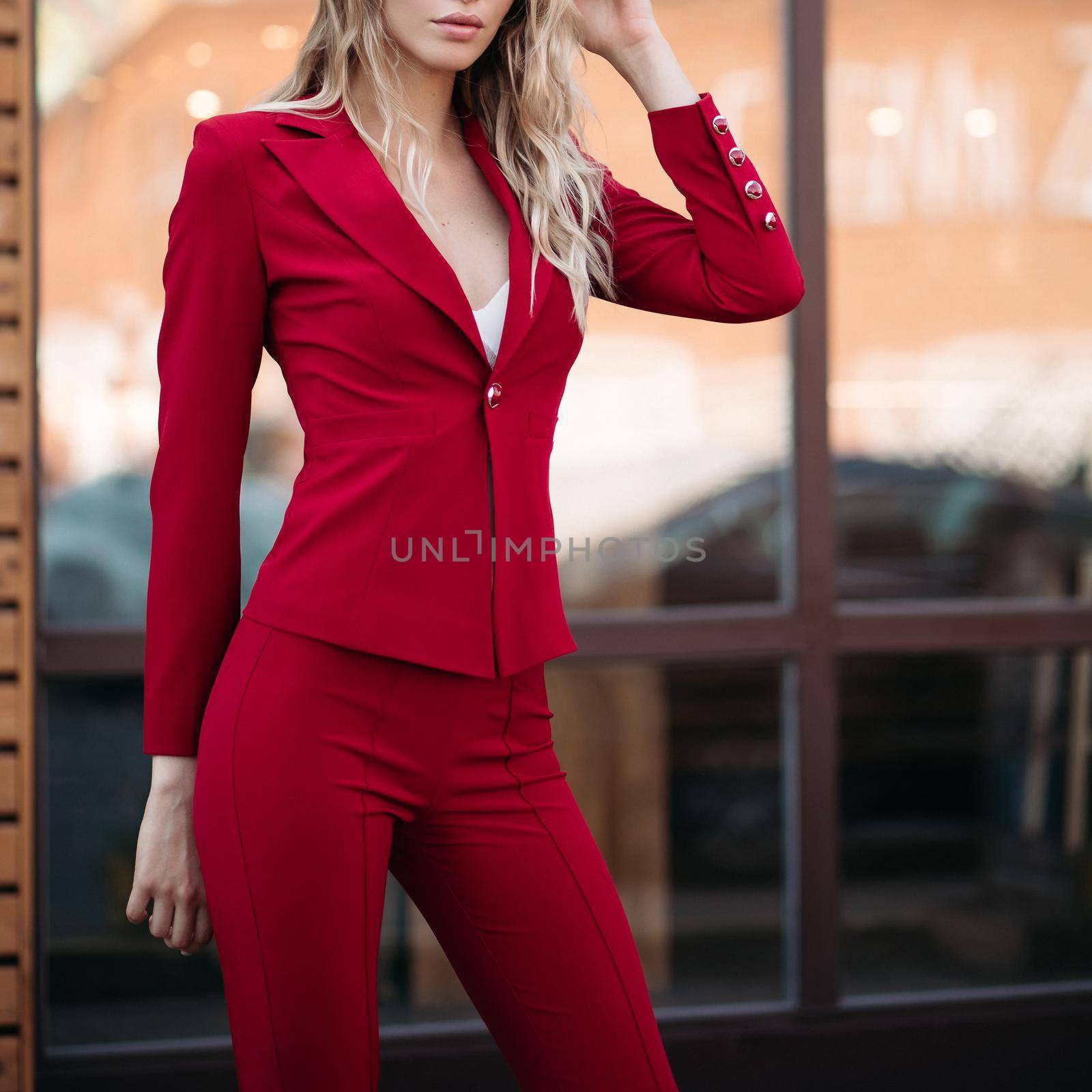 elegant gorgeous blonde businesswoman in expensive dark red jacket and trousers with golden buttons on sleeves. She is standing with arms crossed.