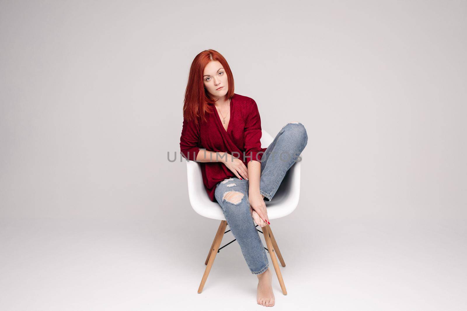Model with ginger hair sitting on white chair in studio. by StudioLucky