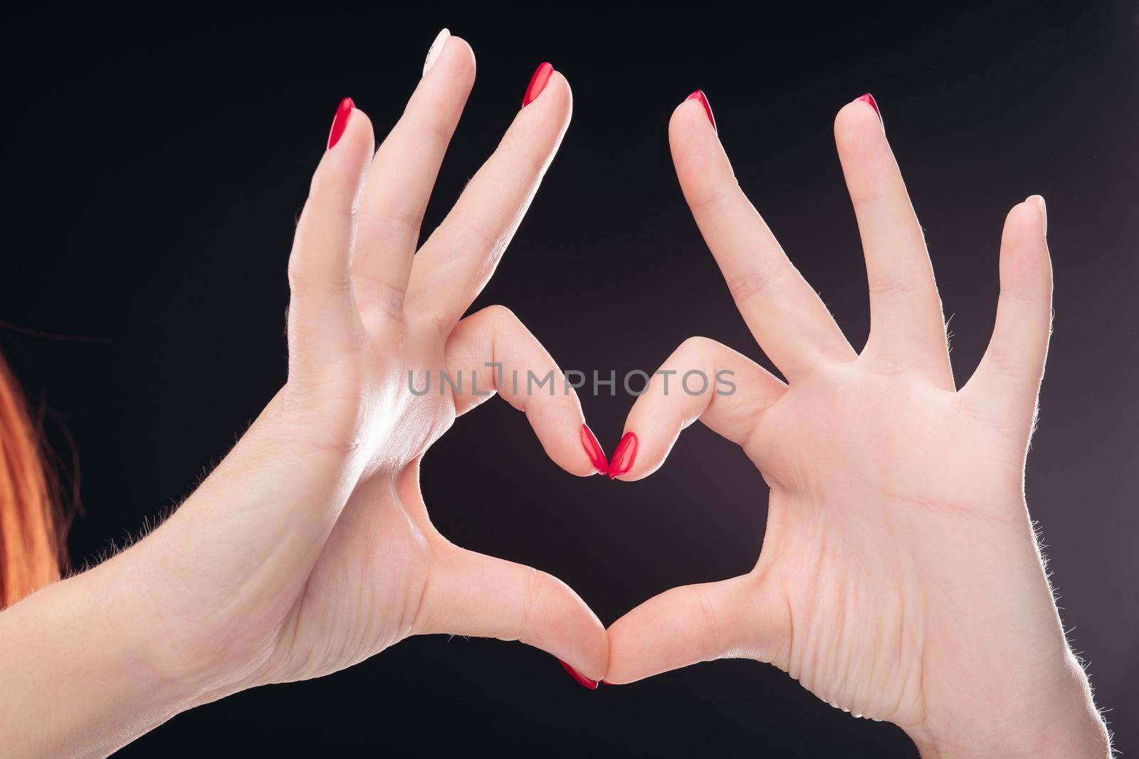 Isolated love sign making by hands with red manicured nails on black studio background. by StudioLucky