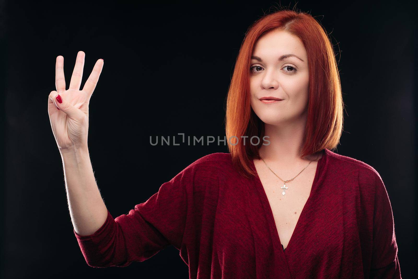 Attractive red haired girl holding hand with 3 finger up. by StudioLucky
