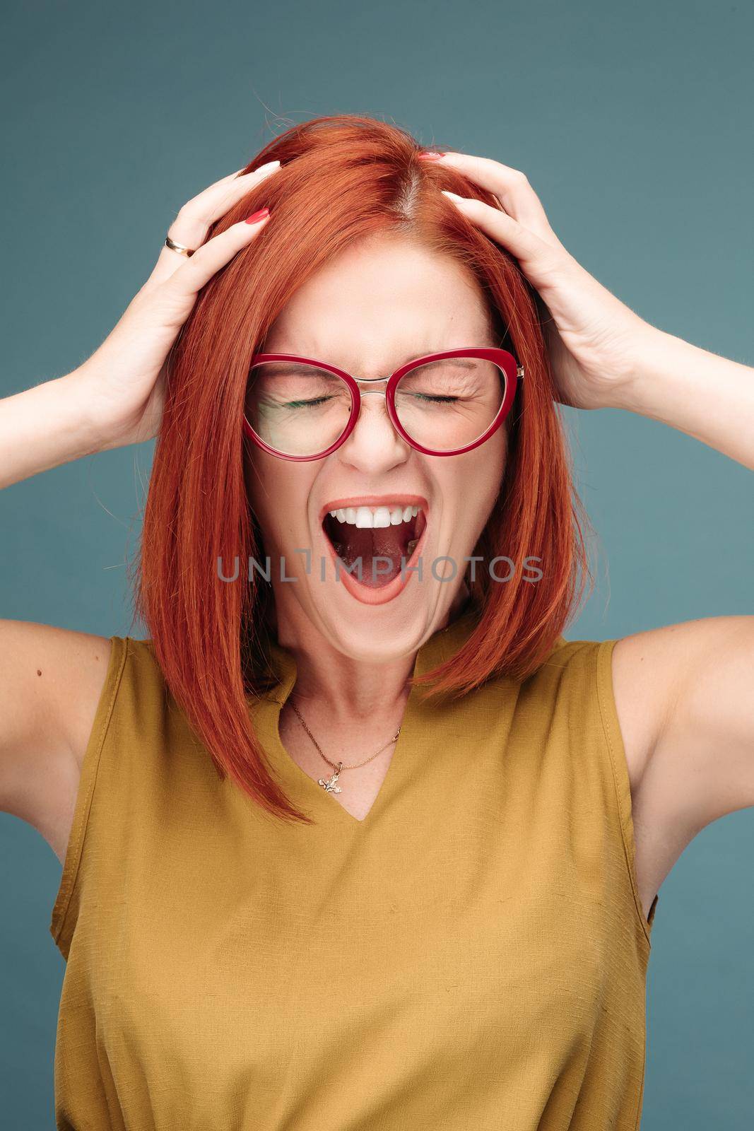 Front view of happy and positivity red haired woman in eyeglasses shouting holding head by hands, looking at camera. Emotionally girl smiling and surprised, having good shock. Drive and happy concept.