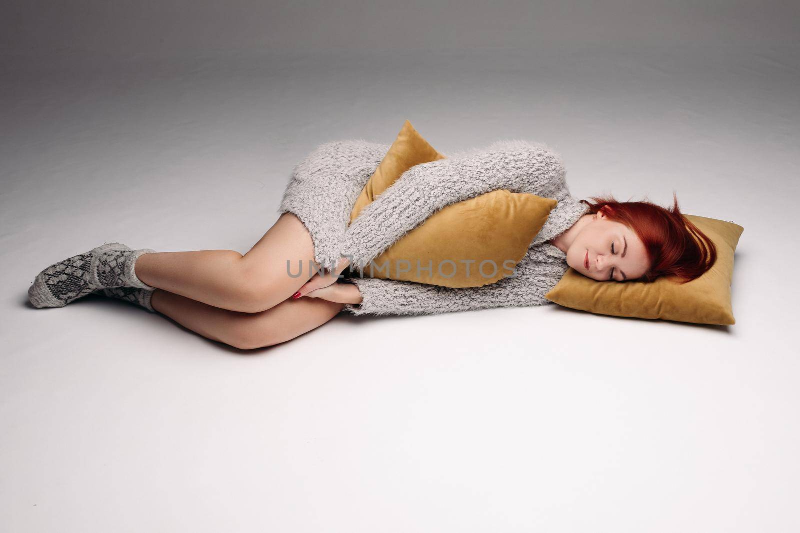Studio portrait of a woman in a sweater hugging a pillow. by StudioLucky