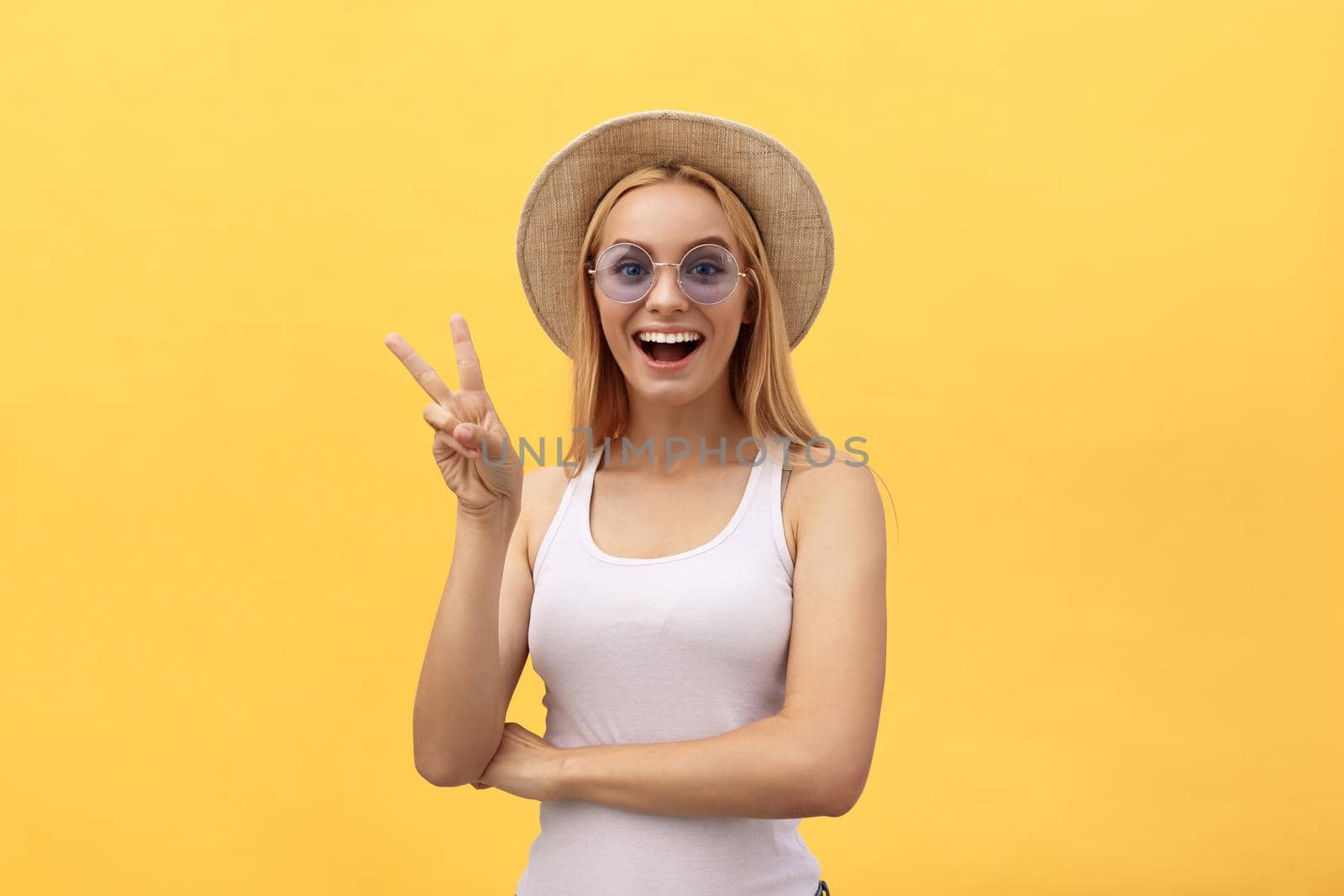Image of cheerful caucasian woman wearing casual clothing smiling and showing peace sign with two fingers isolated over yellow background in studio