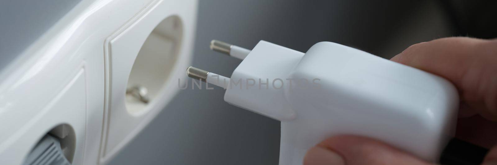 Female hands plug the charger into an outlet in the wall, close-up. Power plug. Electricity in household. Device in socket