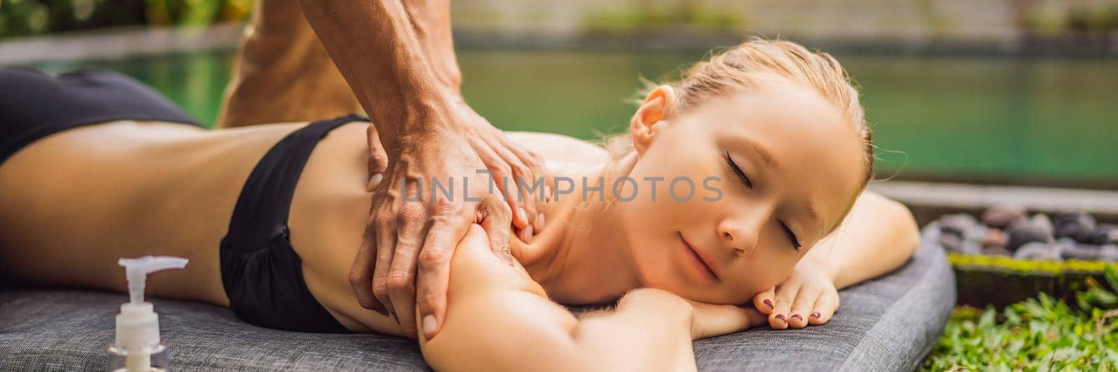 Young woman relaxing outside at a health spa by a swimming pool while having a massage. BANNER, LONG FORMAT