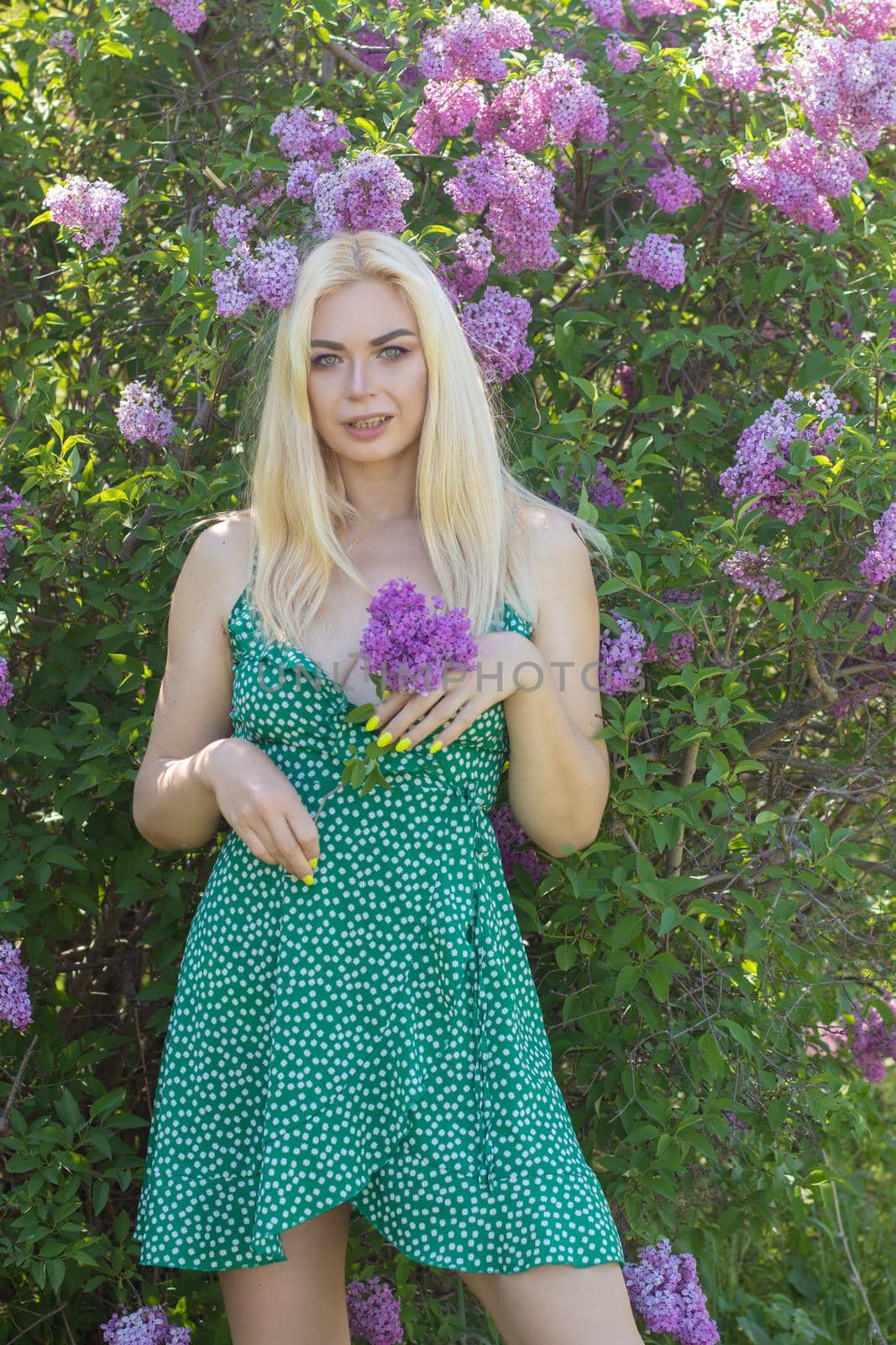 Fashionable girl model near a lilac bush. Spring flowers and beautiful blonde woman. Model appearance. Soft focus