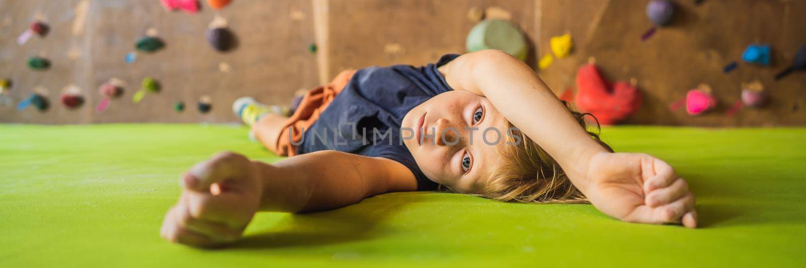 Boy resting after climbing a rock wall indoor. BANNER, LONG FORMAT