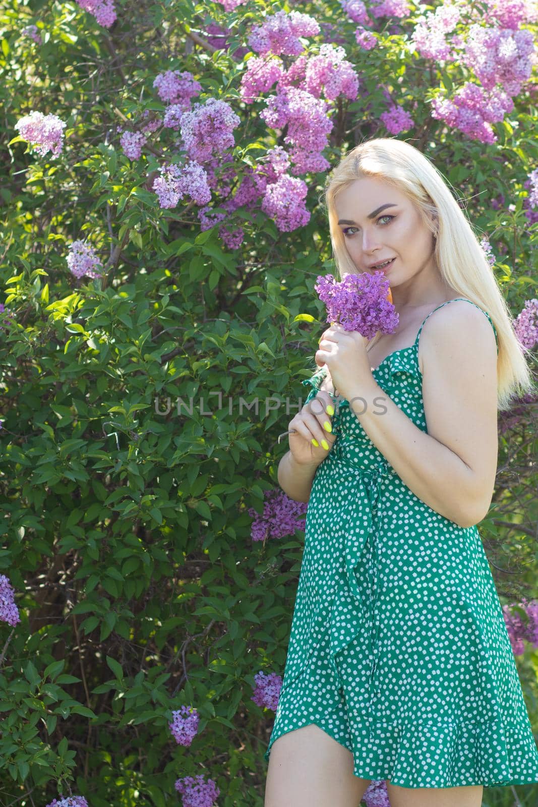 Fashionable girl model near a lilac bush. Spring flowers and beautiful blonde woman. Model appearance. Soft focus