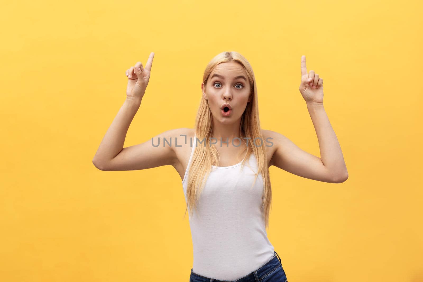 Surprised young woman wearing white clothes while looking at camera isolated on yellow background