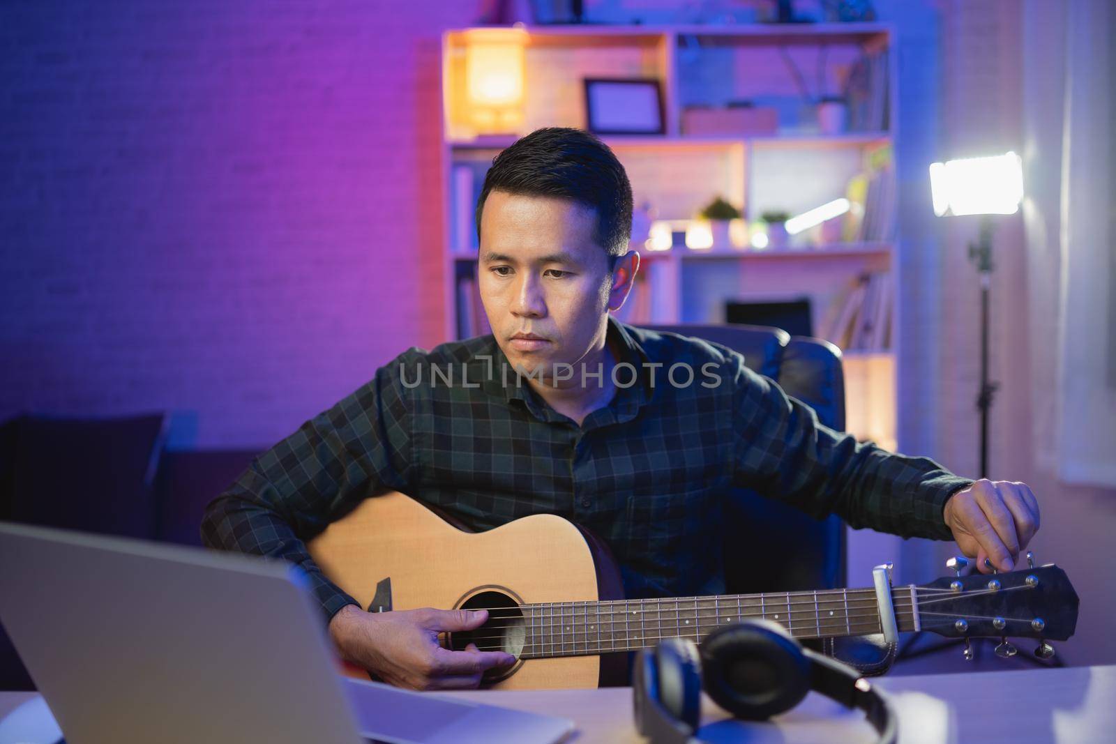 Asian man youtuber live streaming perfomance playing guitar and sing a song. Asian man teaching guitar and singing online. Musician recording music with laptop and playing acoustic guitar.