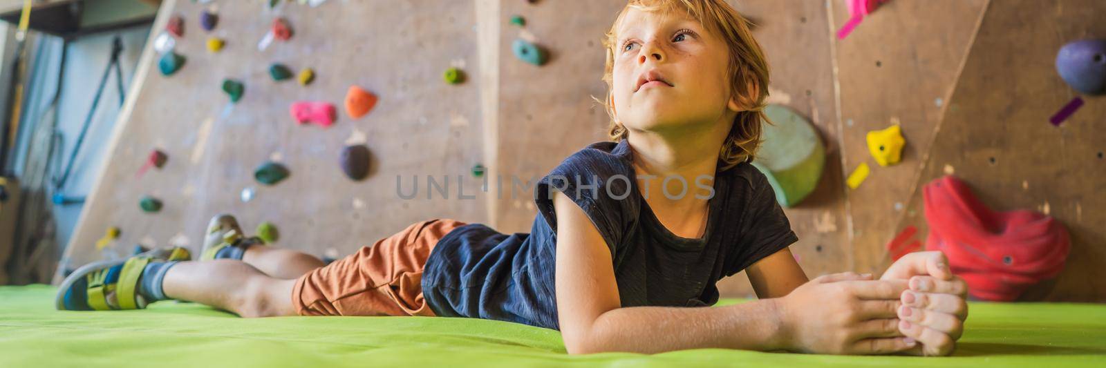 Boy resting after climbing a rock wall indoor. BANNER, LONG FORMAT