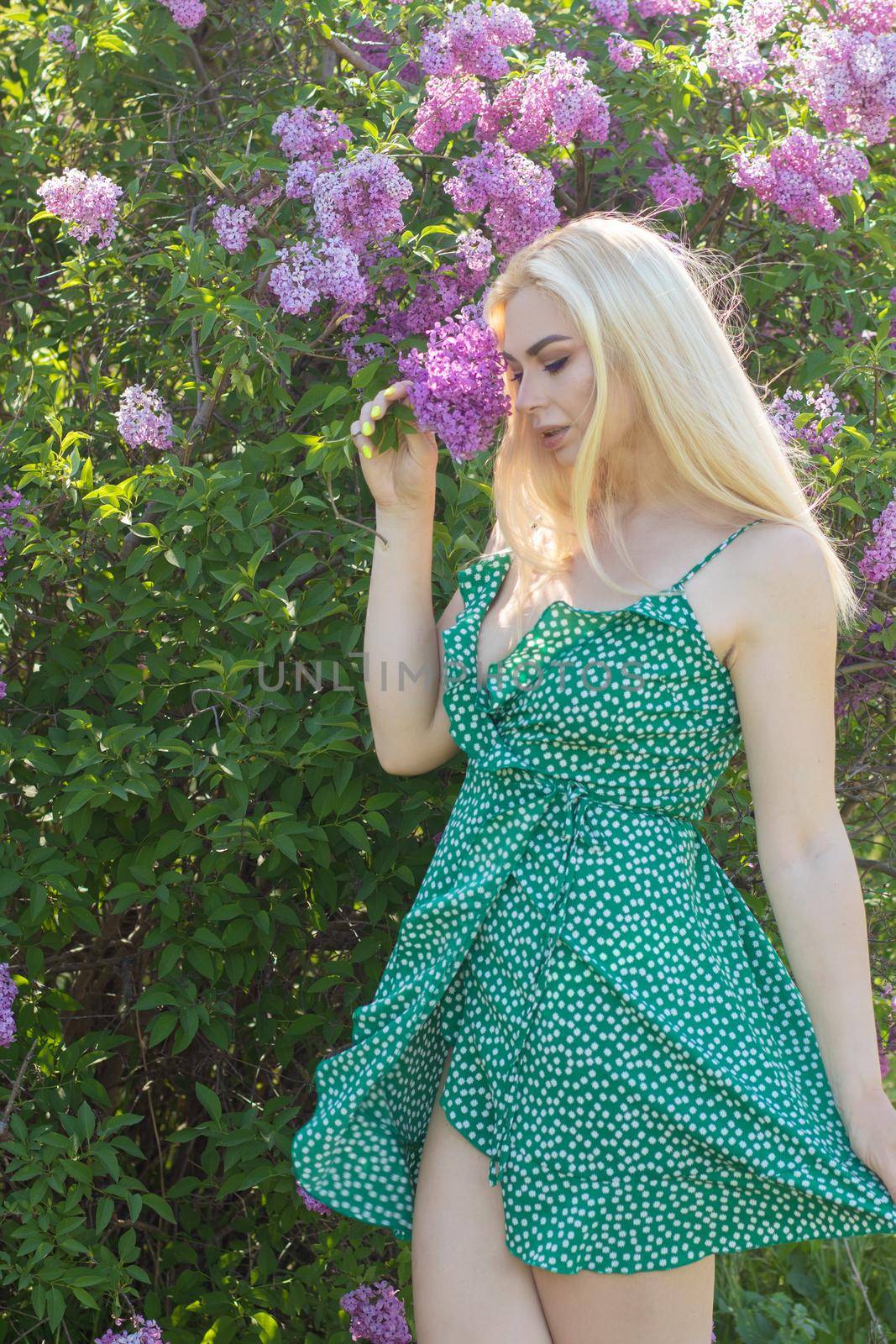 Fashionable girl model near a lilac bush. Spring flowers and beautiful blonde woman. Model appearance. Soft focus