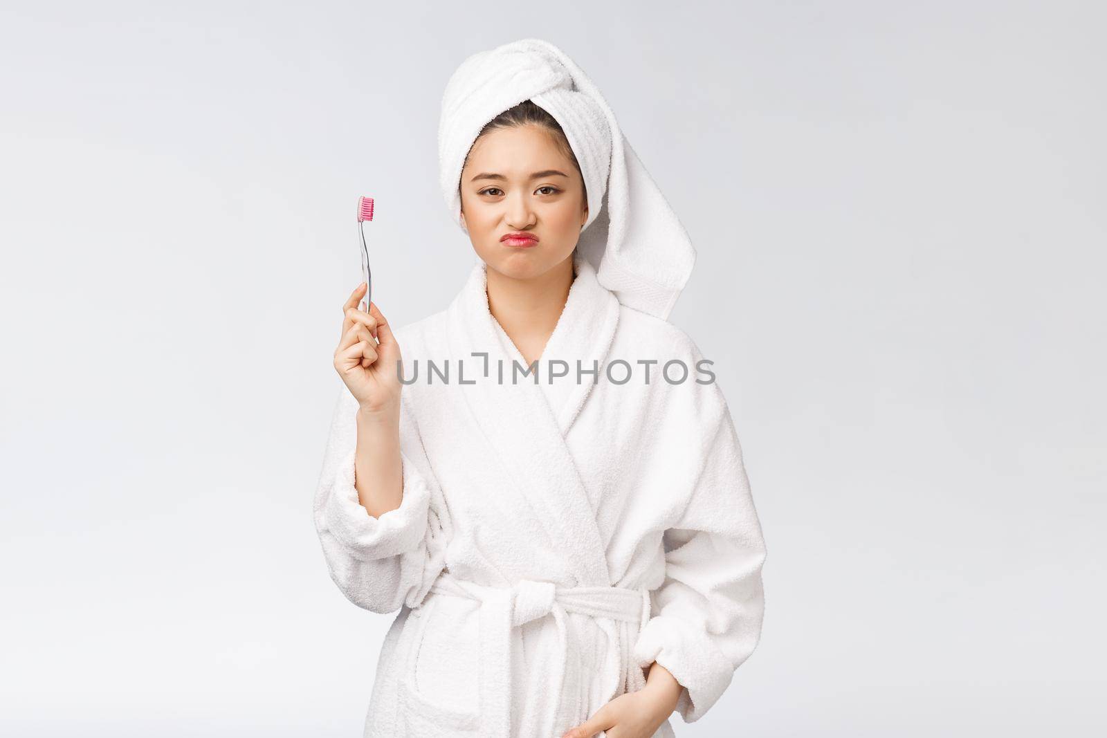 Unhappy beautiful woman brushing her teeth on white background.