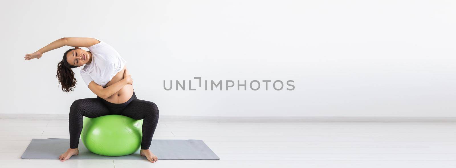 Banner with fexible pregnant woman doing gymnastics on rug on the floor on white background with copy space. Preparing the body for easy childbirth concept by Satura86